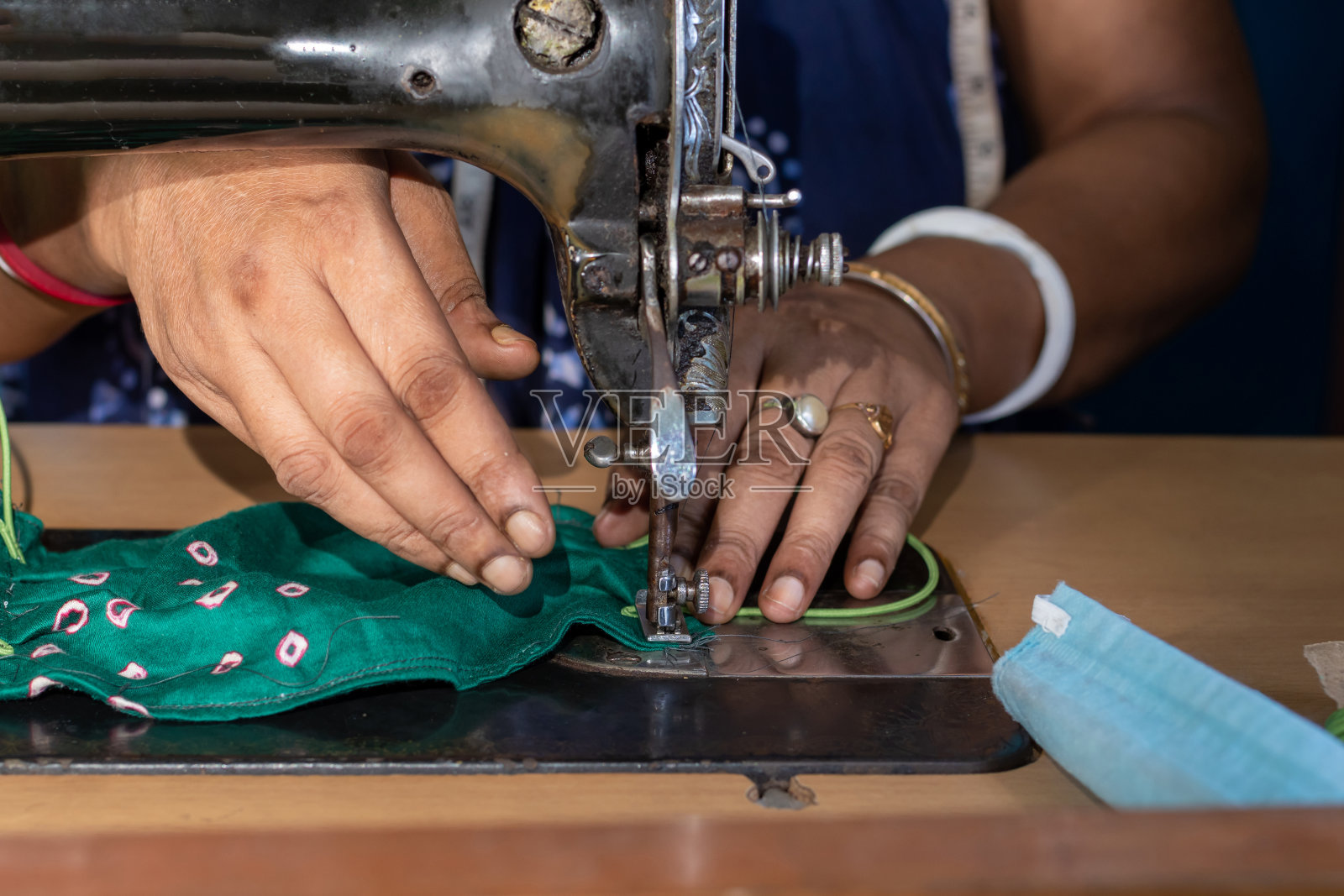 在旧缝纫机上工作的印度妇女——制作自制口罩以防止冠状病毒或新冠病毒传播,移动的针和手指拿着织物的特写细节照片摄影图片