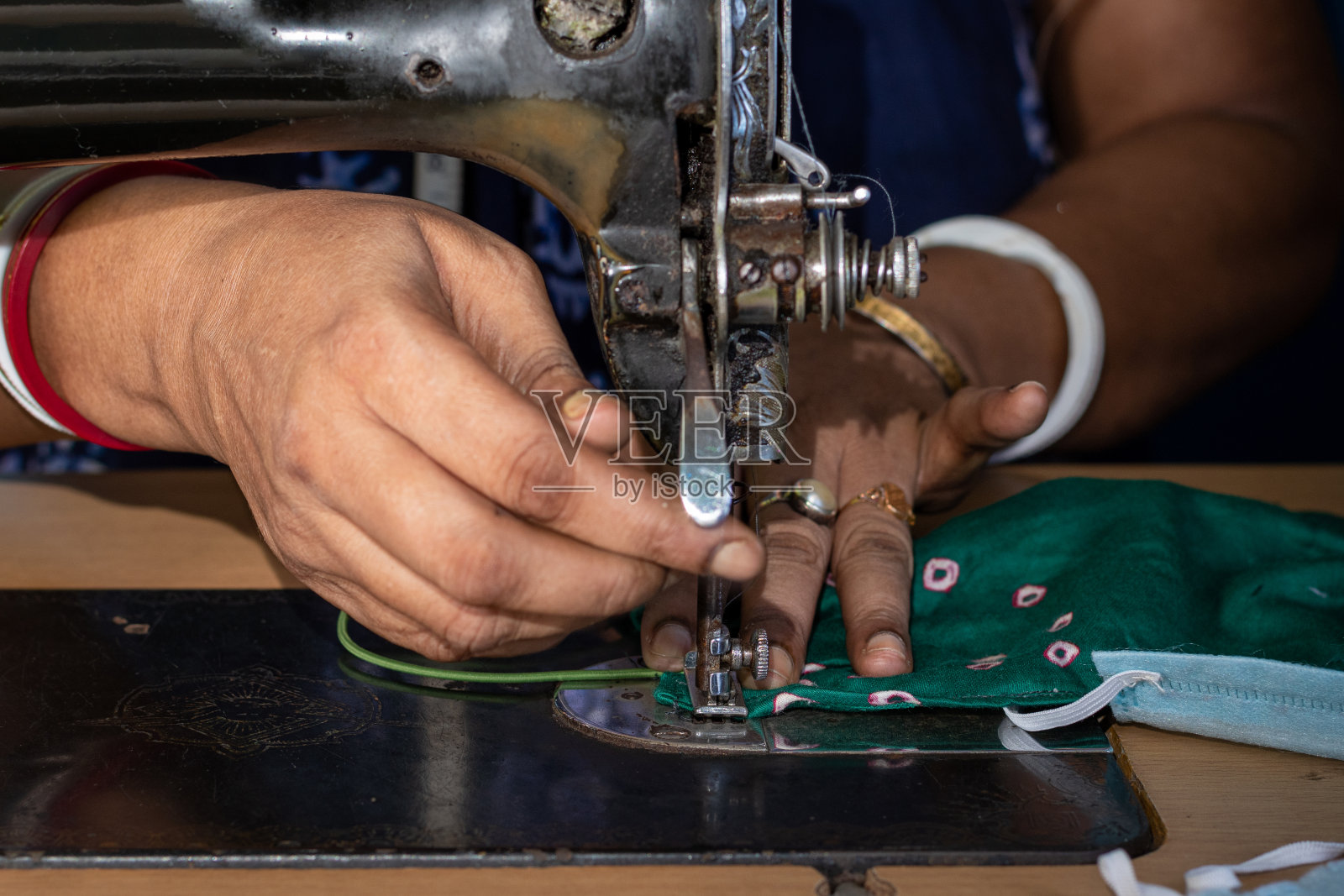 在旧缝纫机上工作的印度妇女——制作自制口罩以防止冠状病毒或新冠病毒传播,移动的针和手指拿着织物的特写细节照片摄影图片