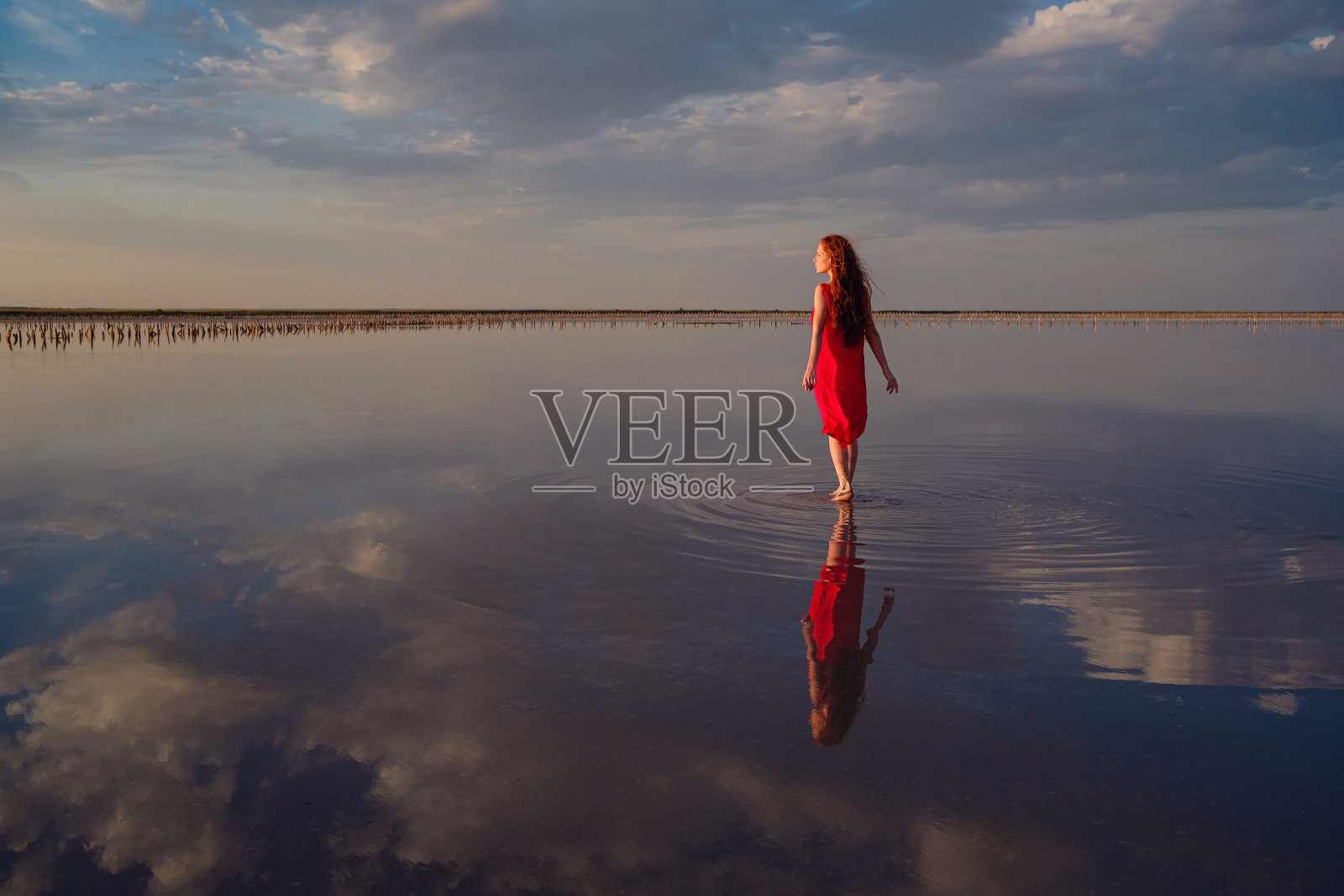 身着红色丝绸连衣裙的优雅女子走过盐湖。照片摄影图片