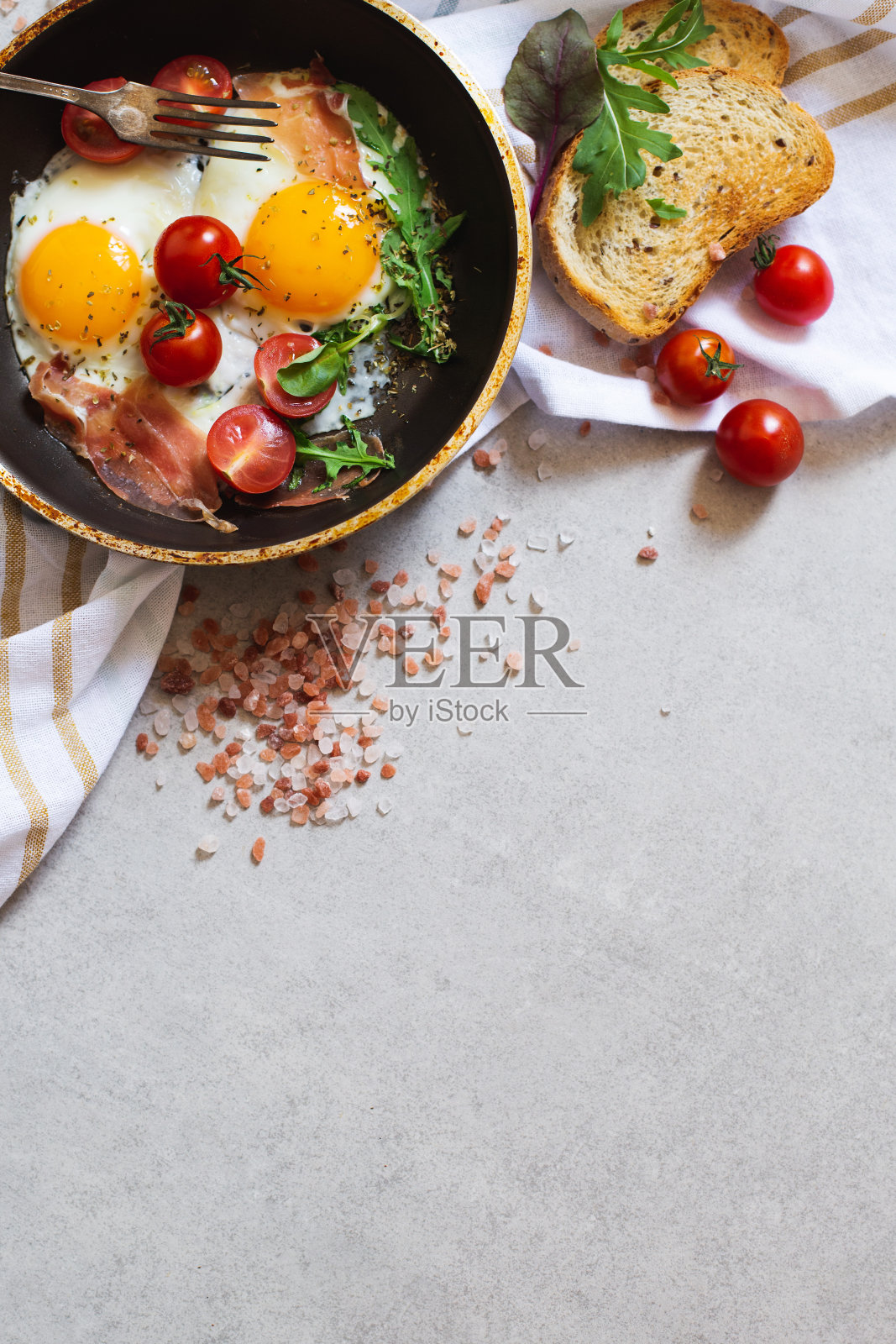 灰色的石头桌上放着炒鸡蛋、培根、蔬菜、樱桃番茄和面包,俯视图照片摄影图片