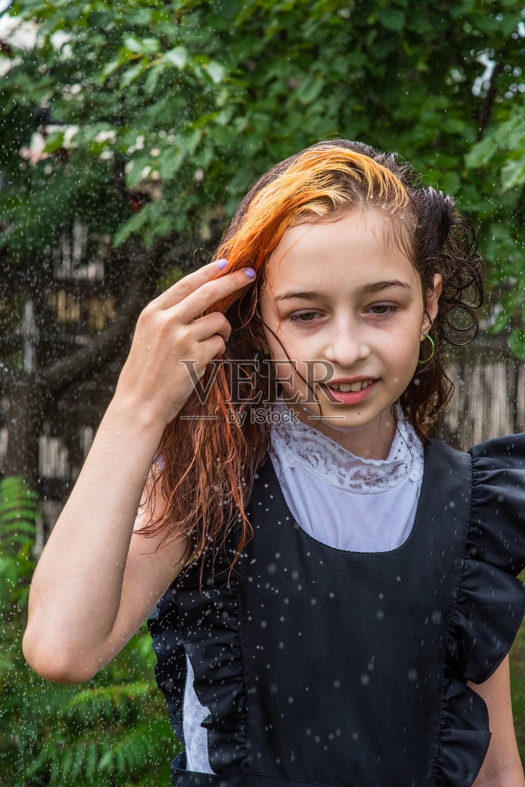 湿漉漉的女生站在雨中。少年在春天或温暖的秋天穿着校服。五年级的女孩。染发。照片摄影图片
