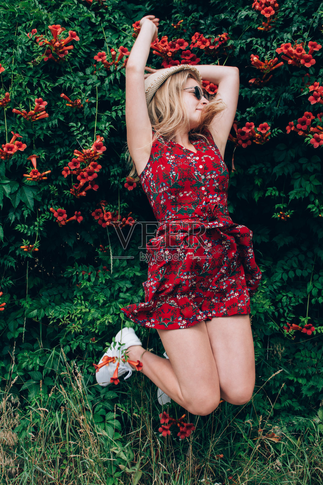 年轻美丽的金发长头发少女在红裙子跳与高举的手在鲜花自然的背景户外照片摄影图片