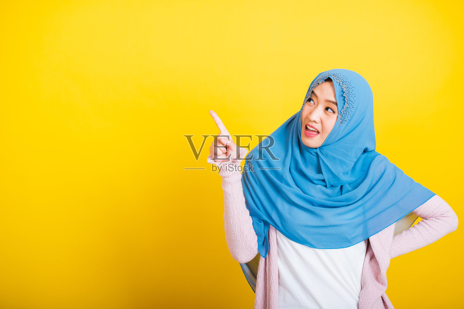 亚洲穆斯林阿拉伯妇女伊斯兰戴着头巾微笑,她积极的表情指着手指一边照片摄影图片