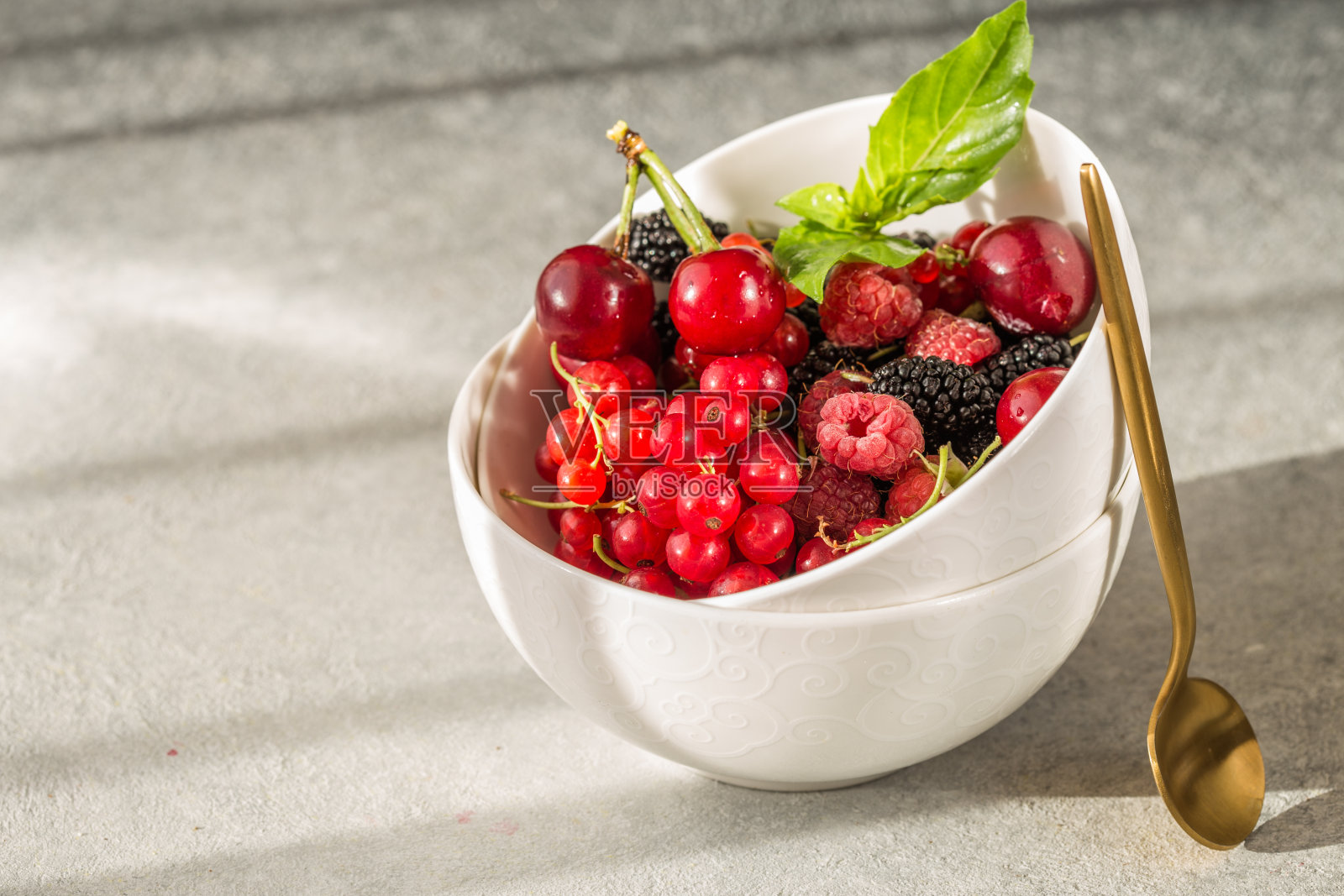 灰色背景上的一碗新鲜浆果。自然强光照片摄影图片