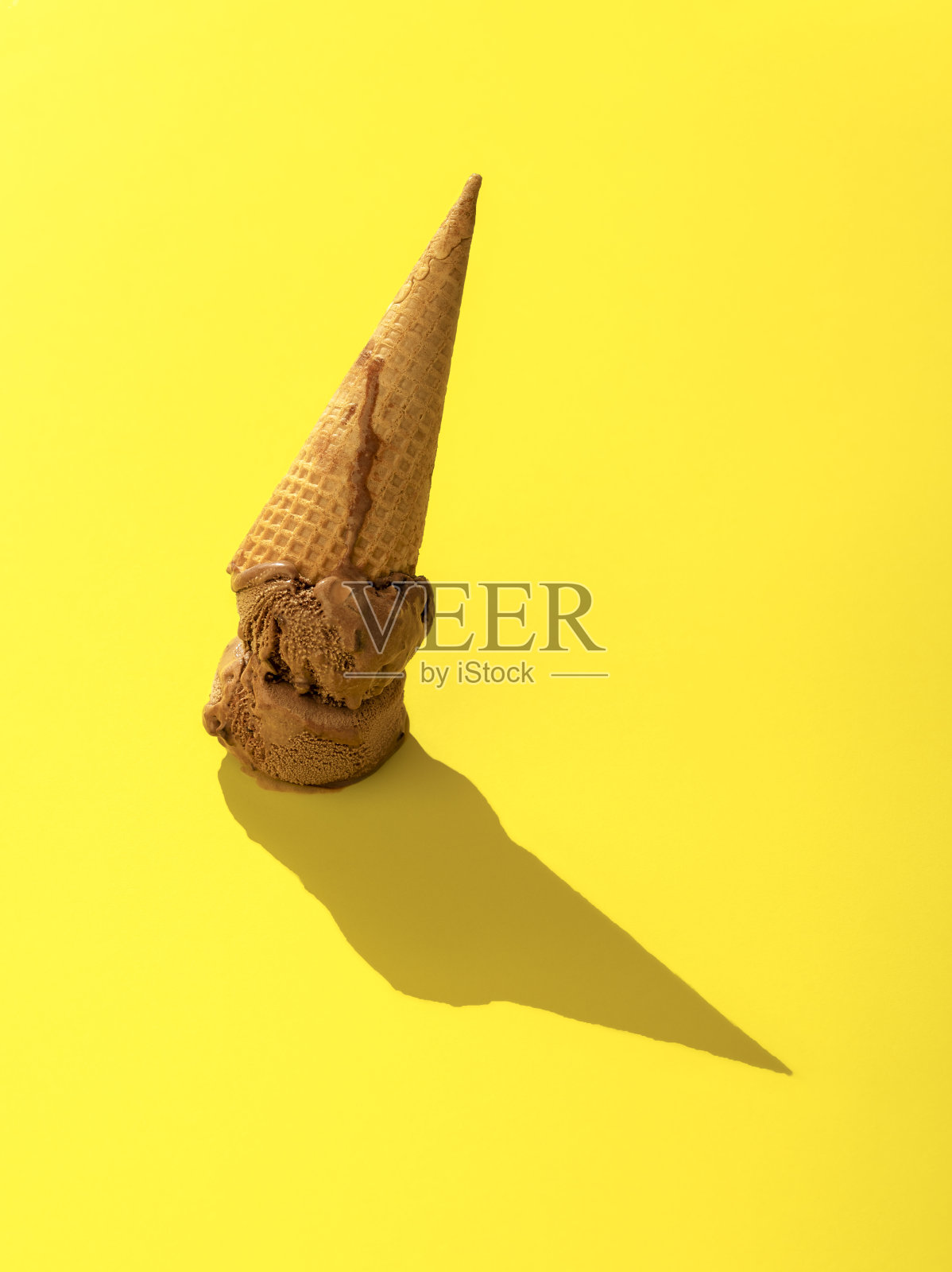 巧克力冰淇淋掉了下来。蛋卷冰淇淋倒挂在黄色背景上。照片摄影图片