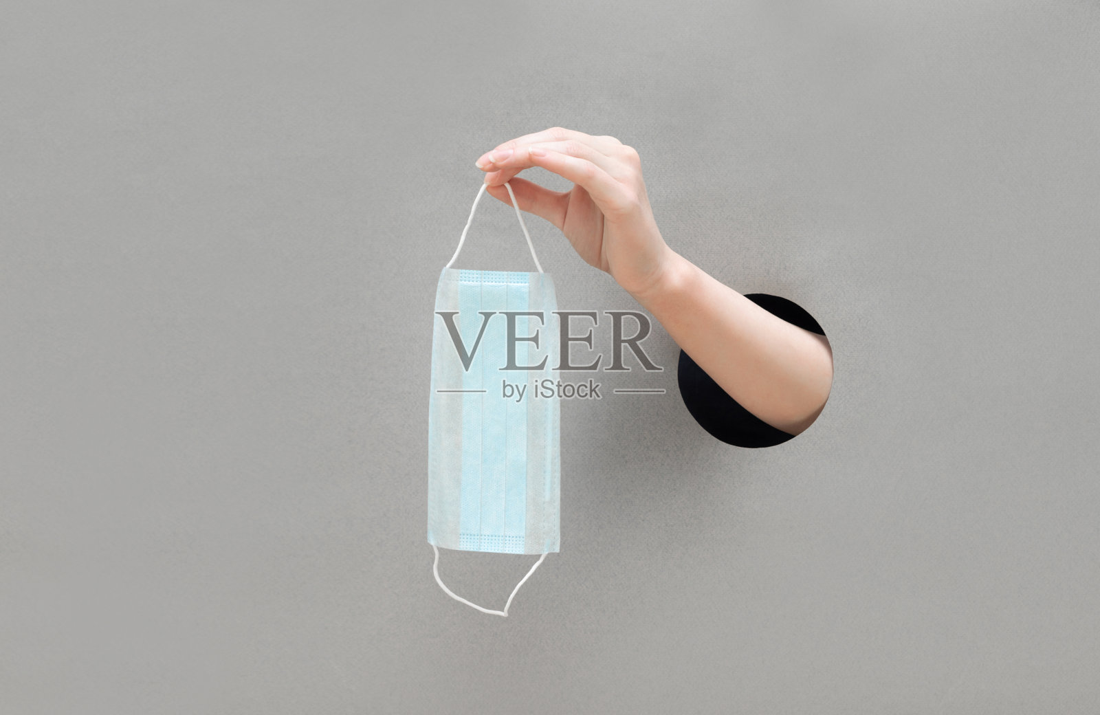 灰色背景下,一位女性手持医用口罩。交一个纸洞。预防冠状病毒、新冠肺炎。照片摄影图片