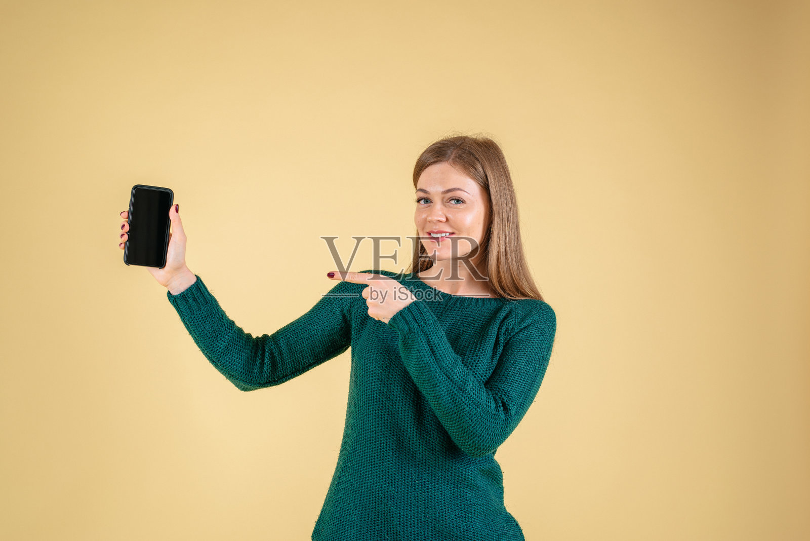 一个快乐的女人的肖像,黄色背景下显示空白的智能手机屏幕照片摄影图片