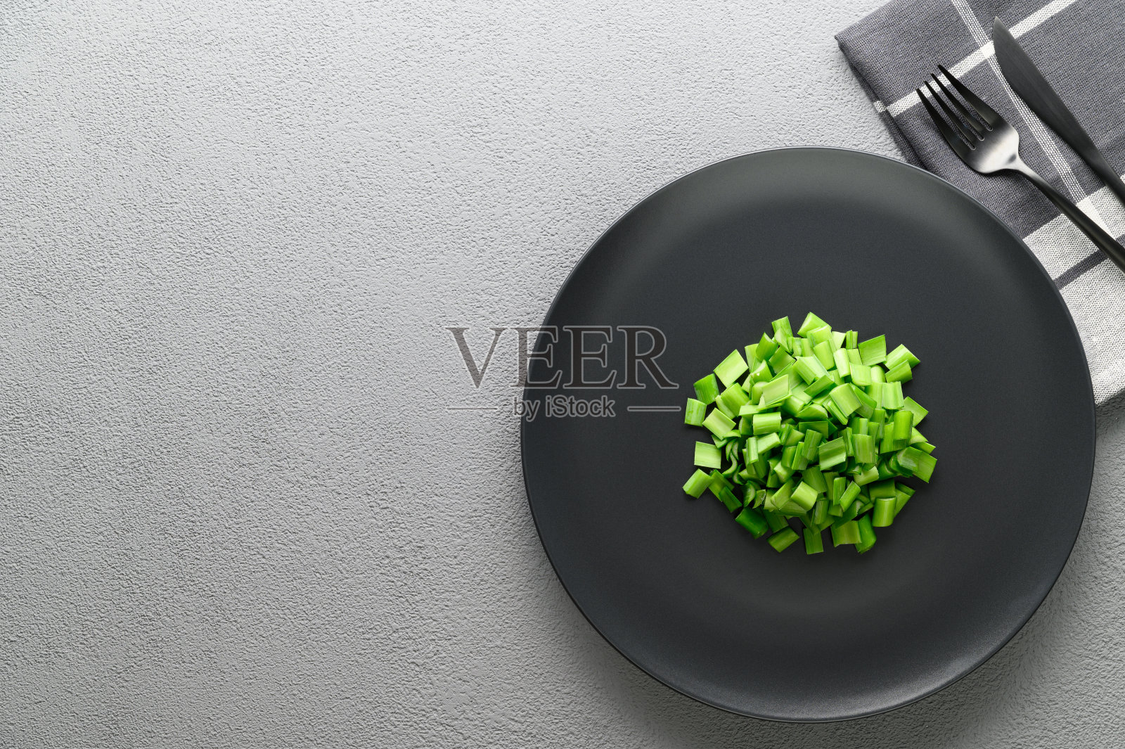 用刀叉把青葱切成薄片放在一个黑色的盘子里。葱属植物高寒洋葱。照片摄影图片