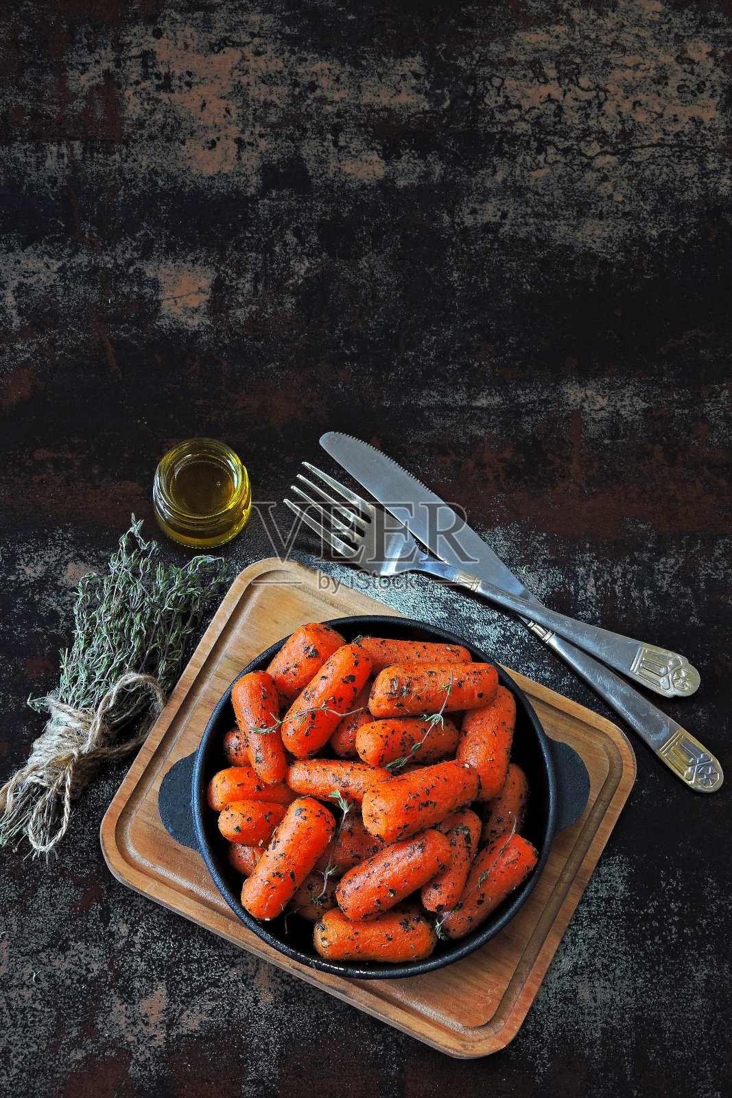 小胡萝卜和香草放在铸铁煎锅里烤。照片摄影图片