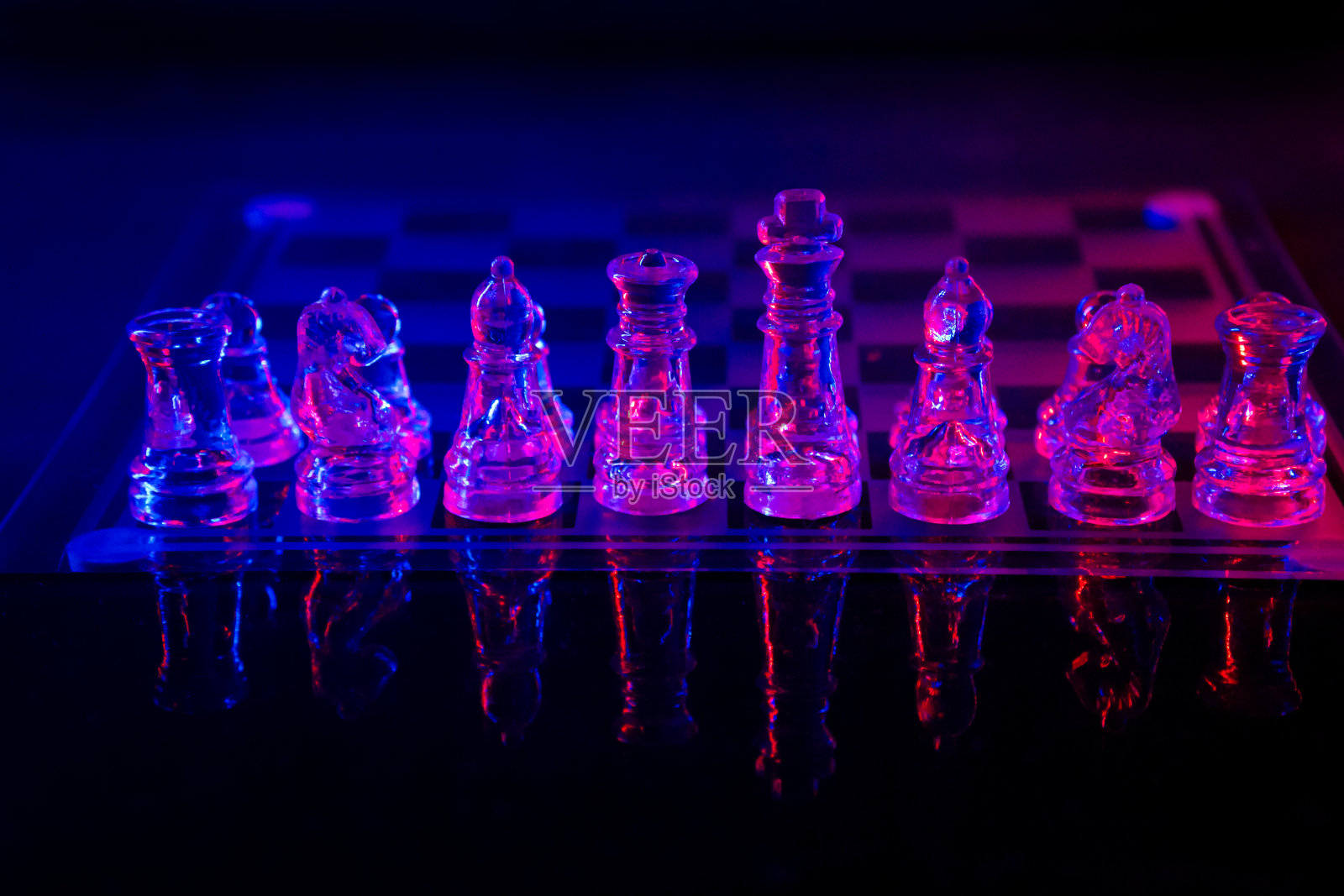 把棋盘上的棋子照在一面被彩色灯光照亮的镜子上。照片摄影图片