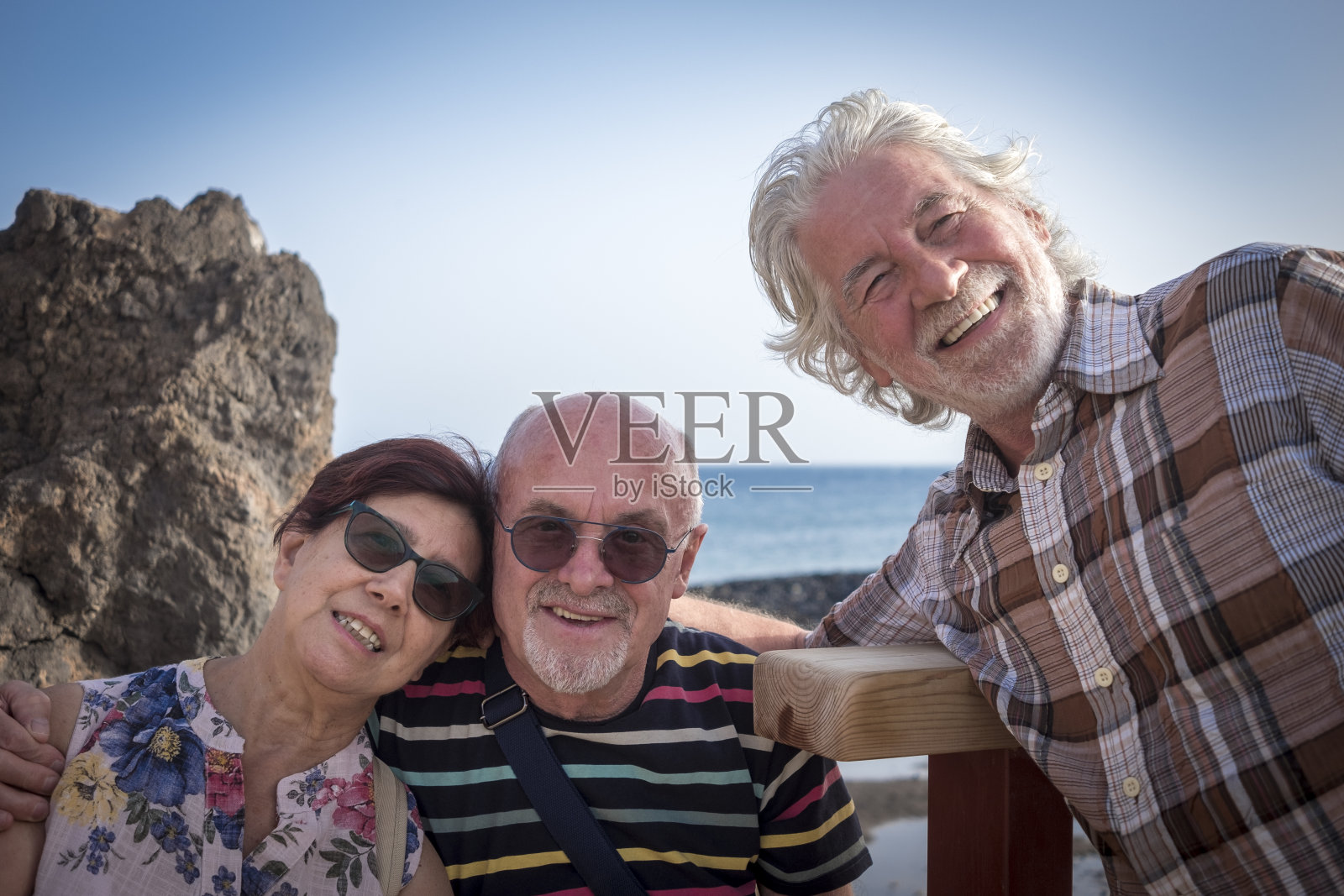 三个快乐的老人微笑着互相拥抱,享受暑假的海上远足——退休期间活跃的老年人的概念——水面上的地平线照片摄影图片