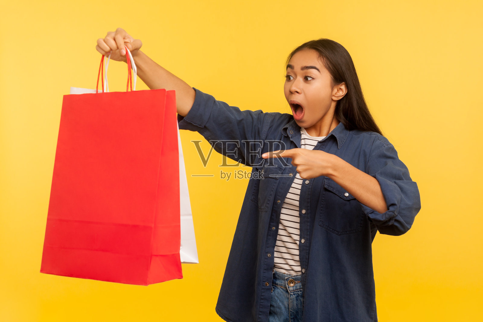 肖像惊讶兴奋的购物女孩在牛仔衬衫指向袋子看起来震惊,惊讶的疯狂购物照片摄影图片