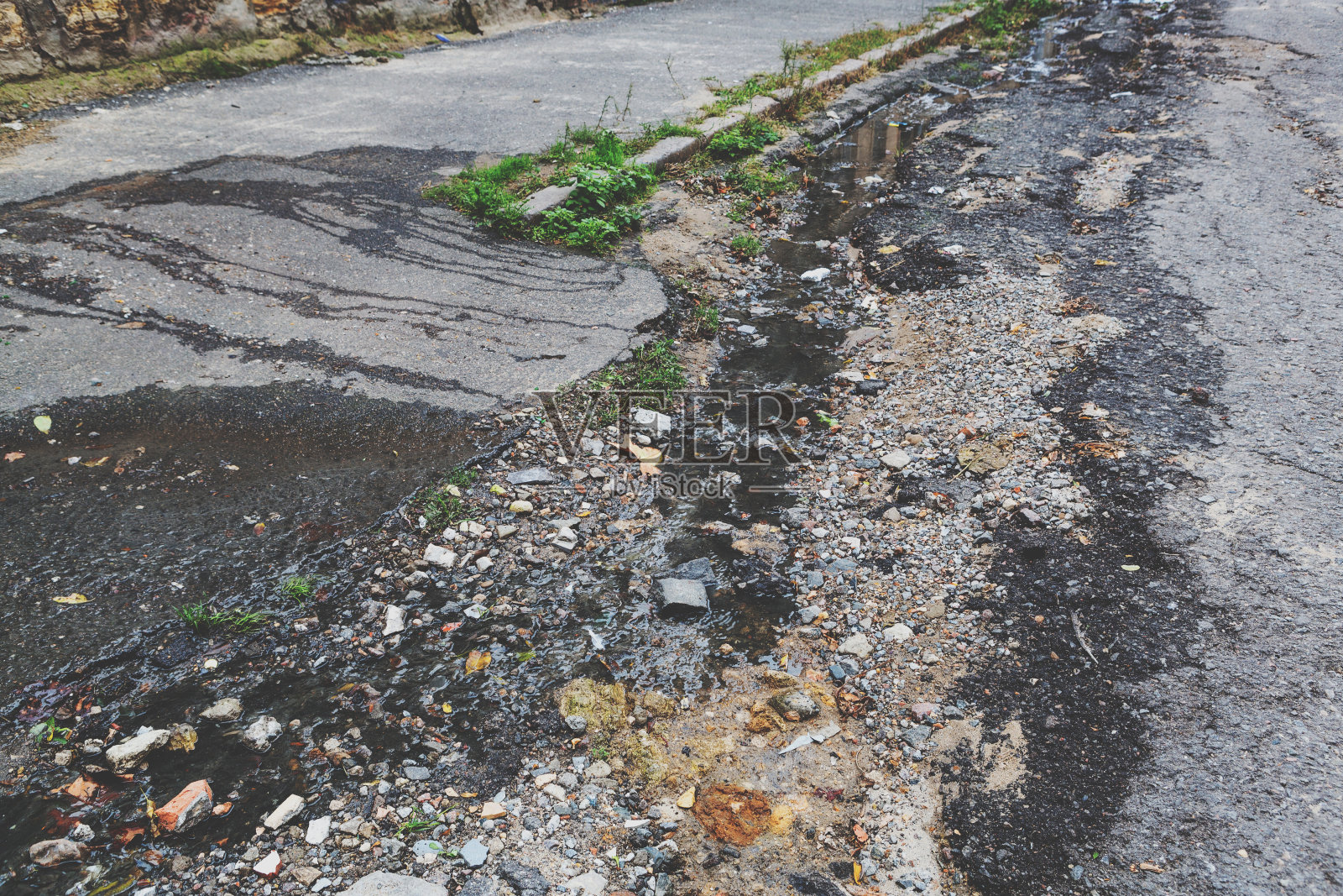 被雨雪损坏的需要维修的道路。破碎的沥青路面造成坑洞,对车辆造成危险。照片摄影图片