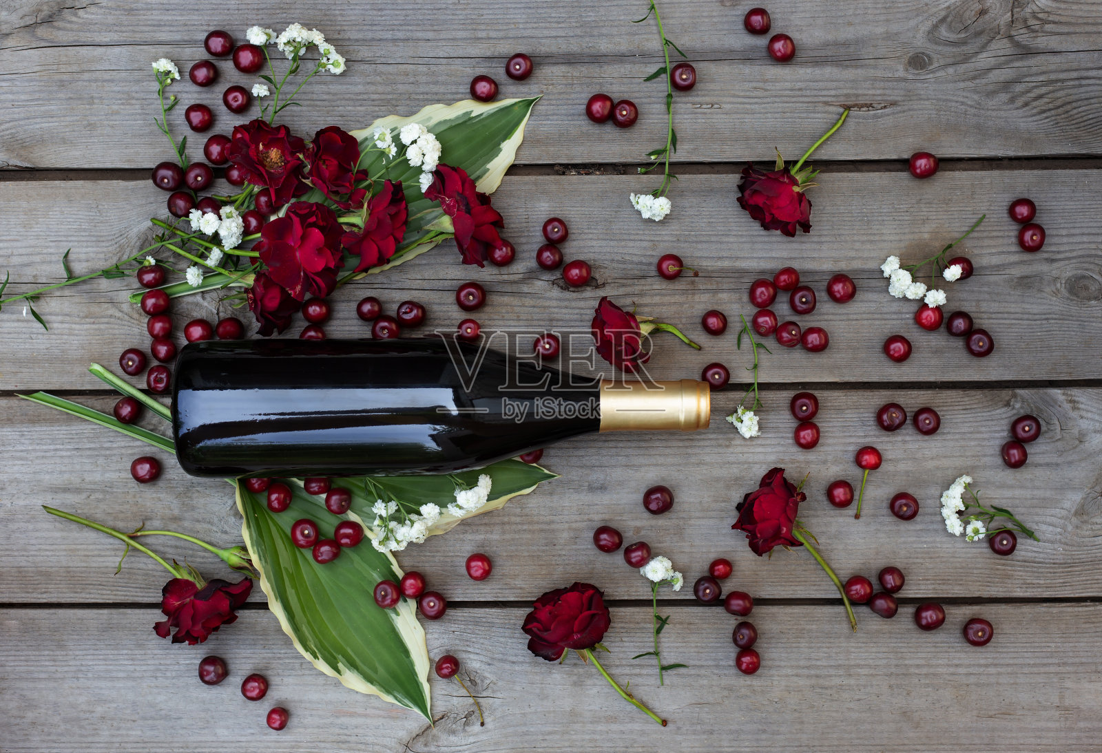 桑格利亚汽酒的成分。木桌上放着一瓶葡萄酒,樱桃和红玫瑰照片摄影图片