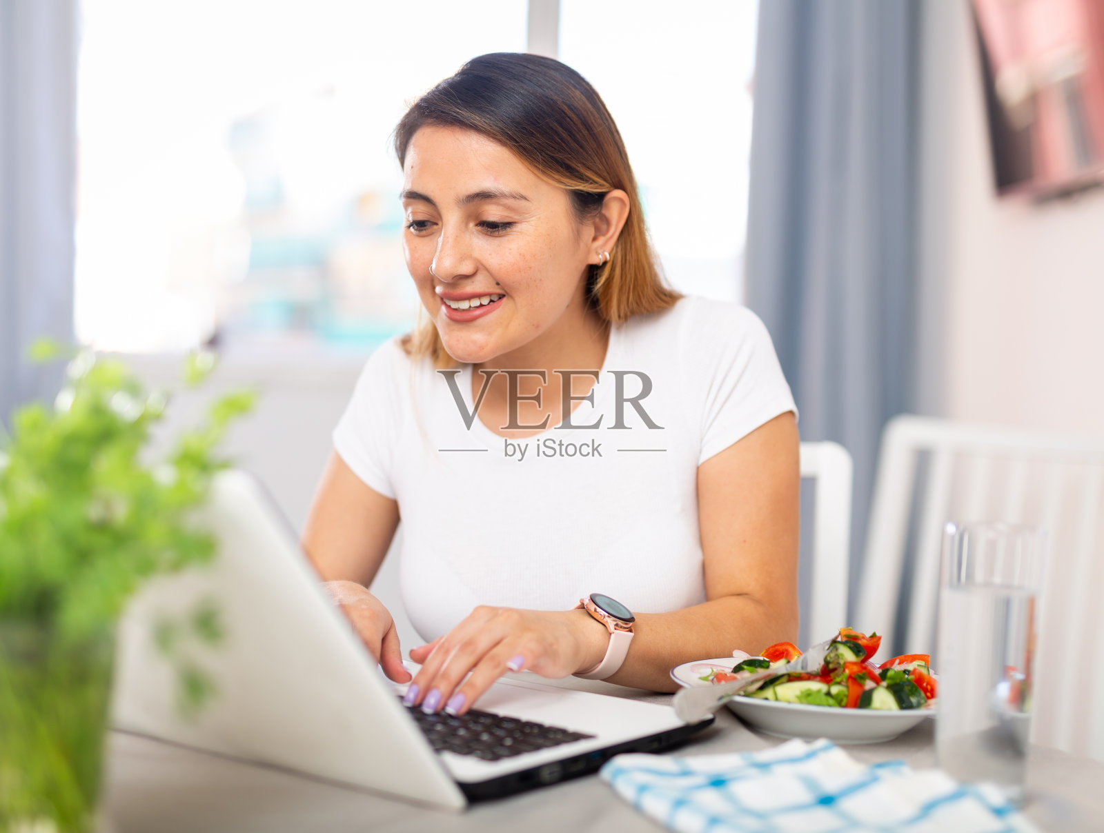 微笑的女人是工作与笔记本电脑坐在桌子和吃沙拉照片摄影图片