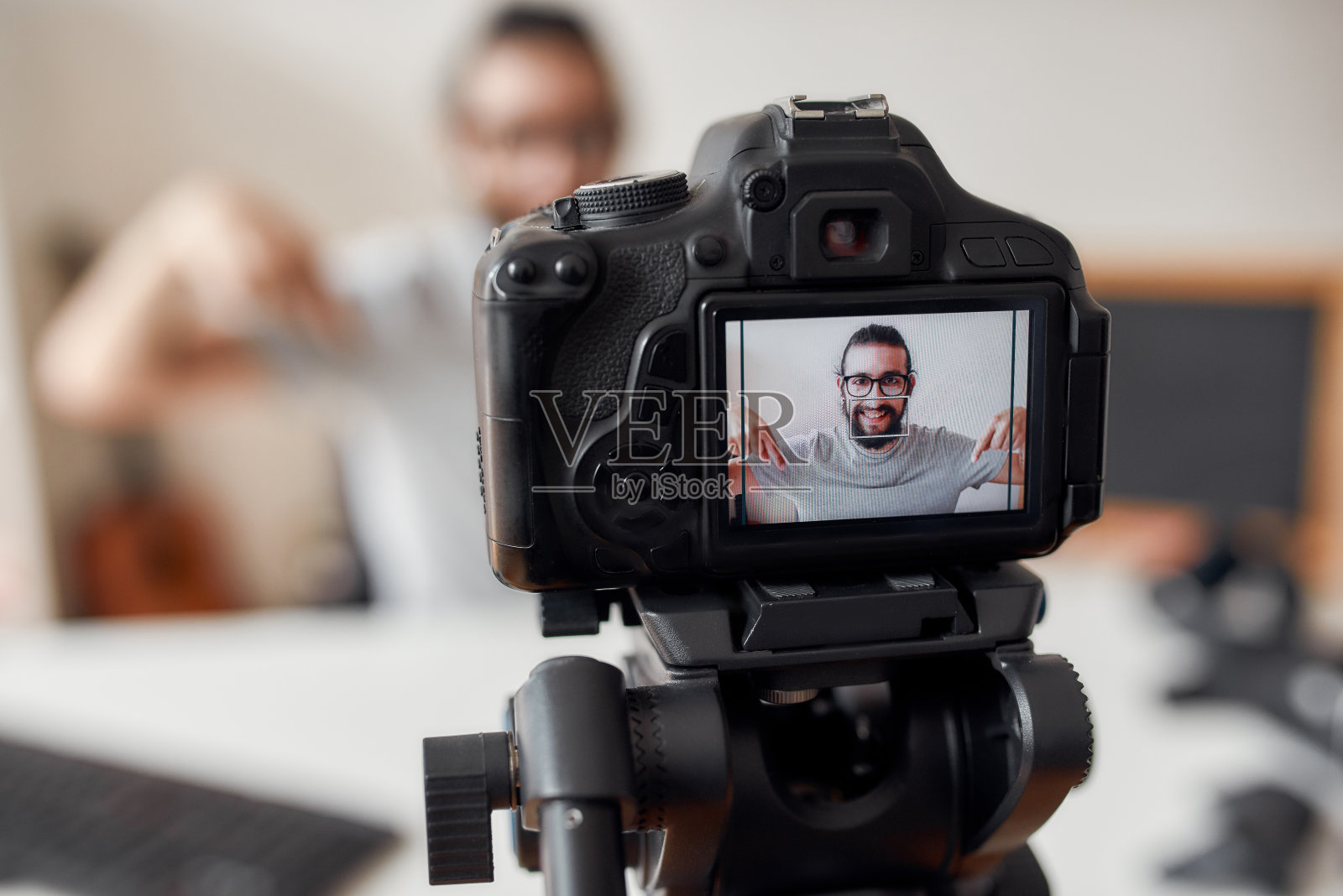 年轻的男性博主指着下面,要求追随者订阅,同时在家庭工作室录制视频博客或vlog。聚焦摄像头屏幕照片摄影图片