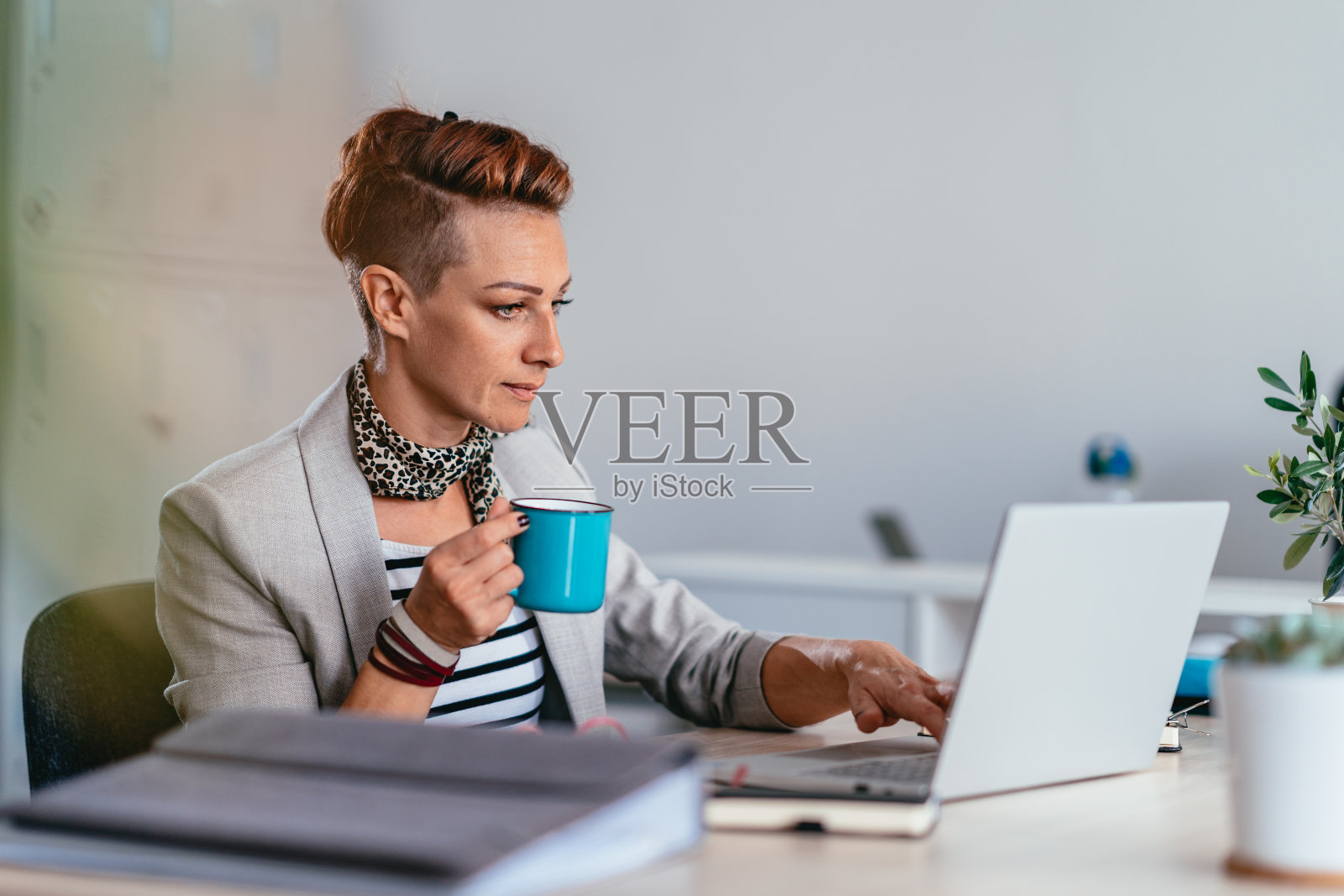 在办公室喝咖啡用笔记本电脑的女商人照片摄影图片