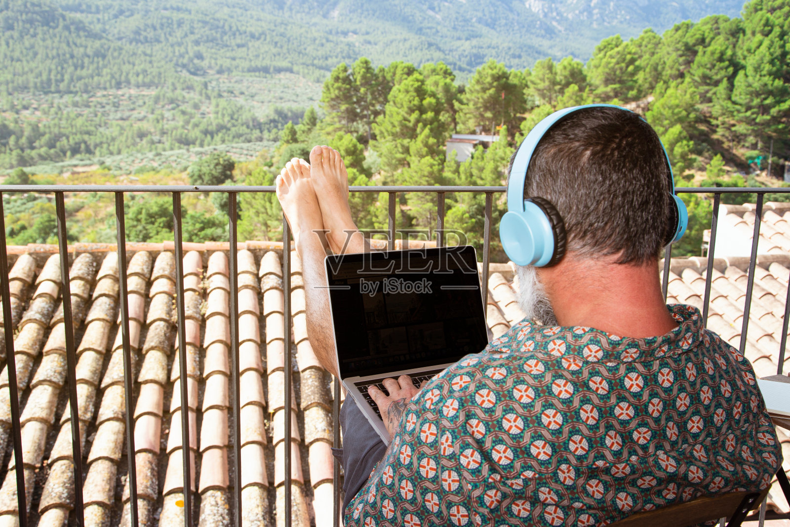 一名男子在自家阳台上戴着耳机用笔记本电脑工作。自由工作者,远程工作,科技,享受阳台。呆在家里。隔离COVID-19时期。照片摄影图片