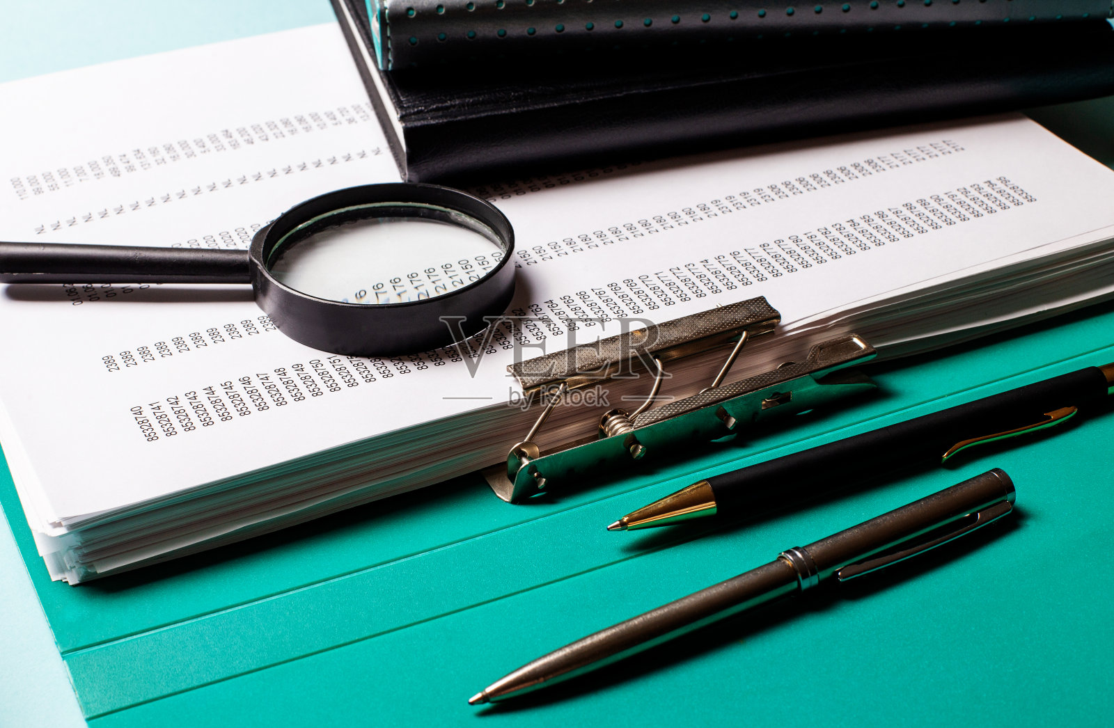 蓝色的桌子上堆放着文件,还有一个放大镜和回形针照片摄影图片