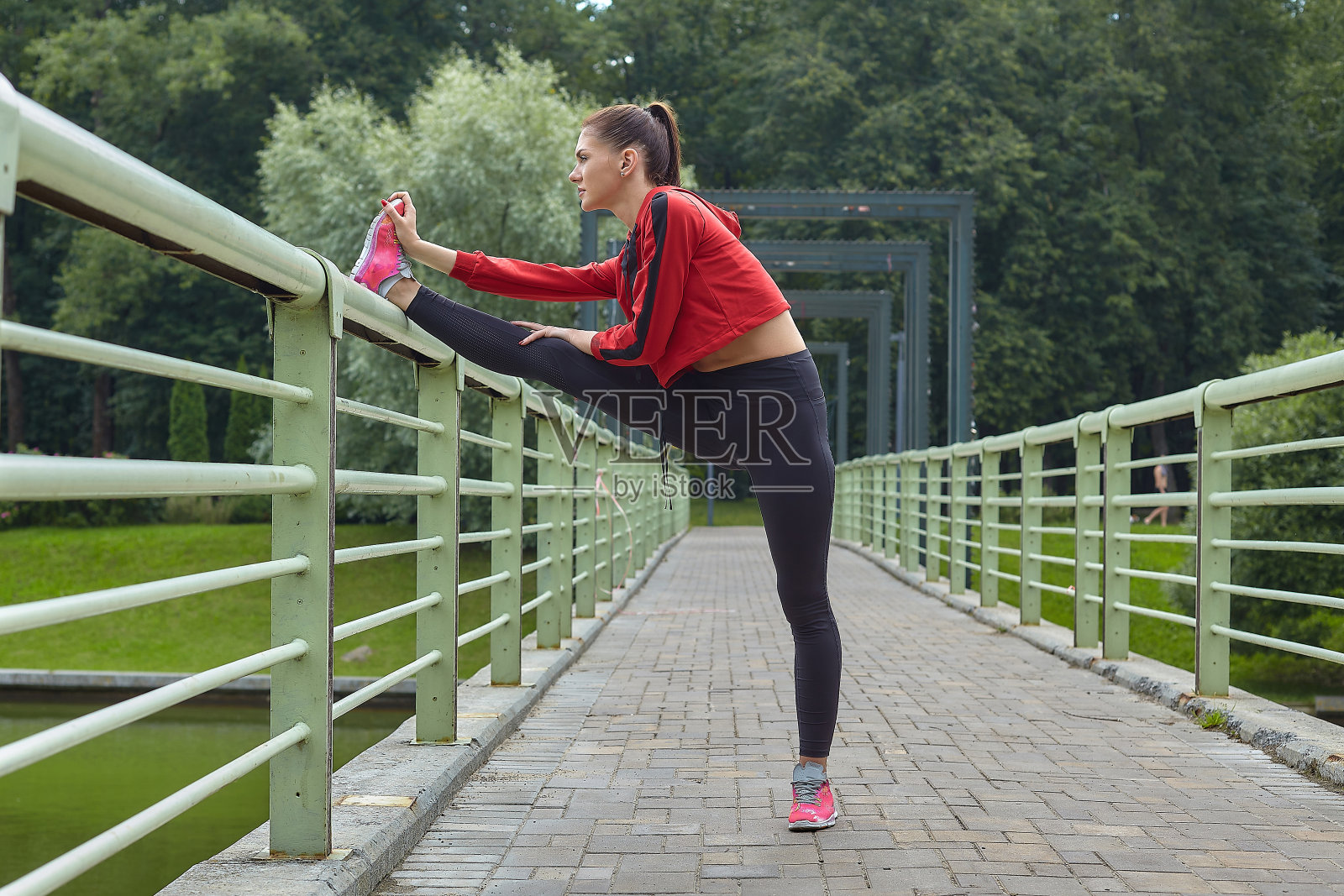 迷人的女孩穿着运动服在城市公园的桥上做热身运动。照片摄影图片