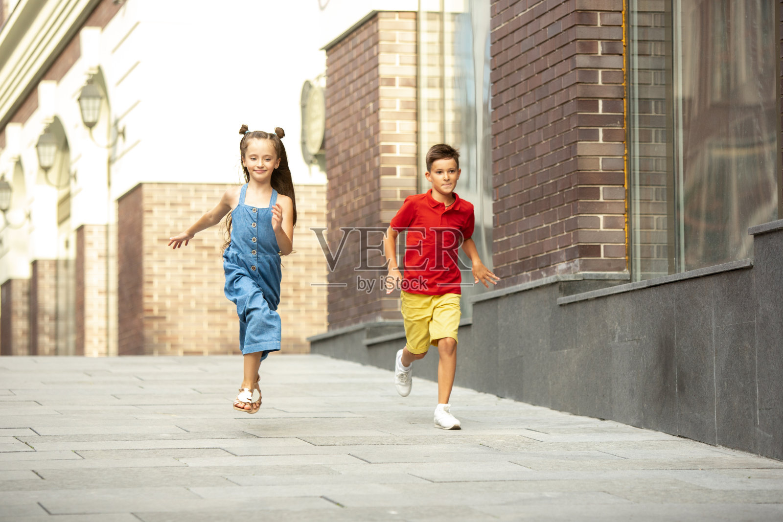 两个微笑的孩子,男孩和女孩一起跑在城里,在夏天的一天照片摄影图片