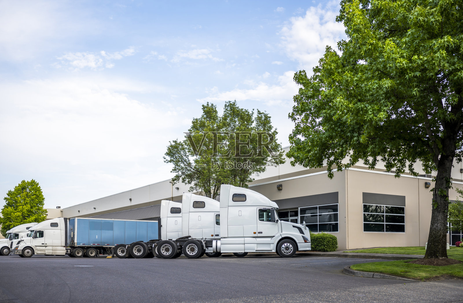 大型钻机、半卡车和半挂车在仓库附近的停车场上排成一排照片摄影图片