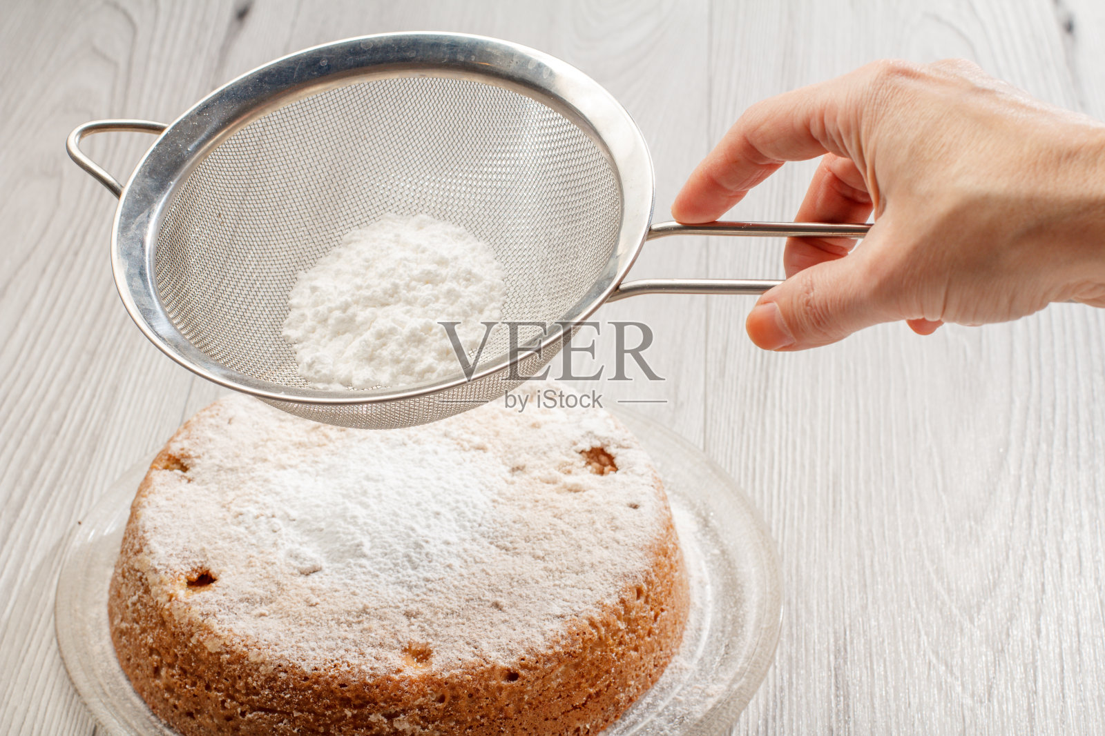 女手里拿着一个筛子,上面撒着糖粉,上面是自制的苹果派照片摄影图片