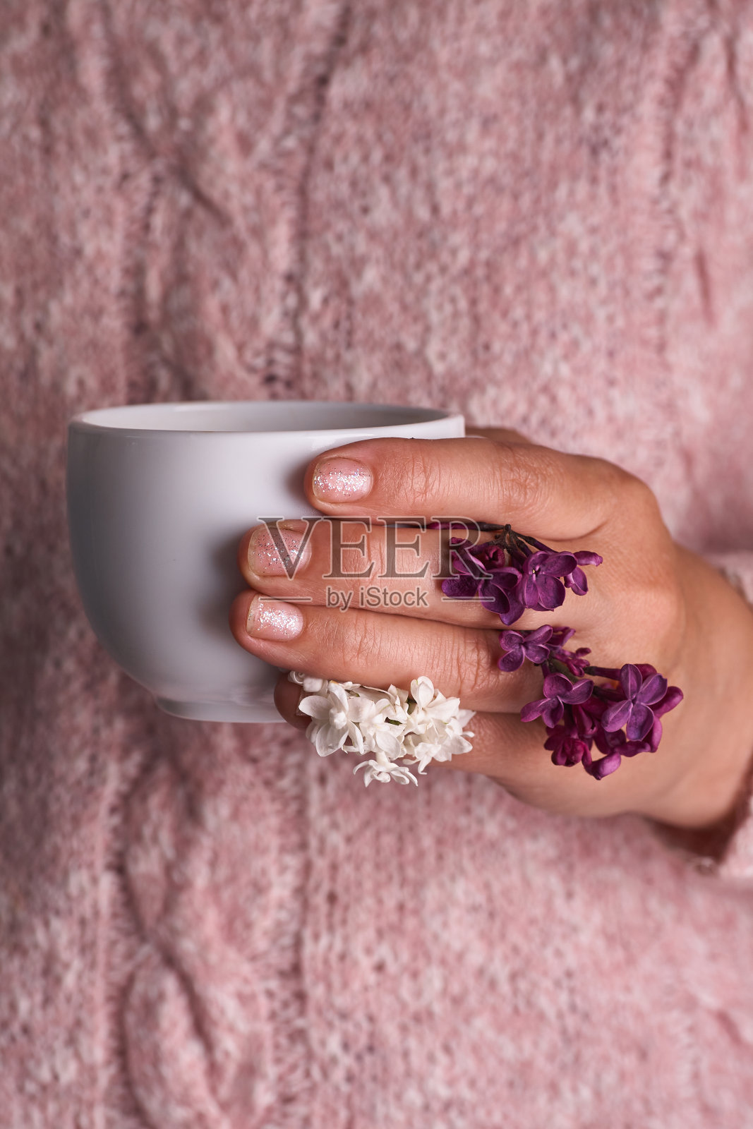 女人的手拿着一杯白色的咖啡。带着一朵美丽的丁香花。早上喝,时尚,照片摄影图片