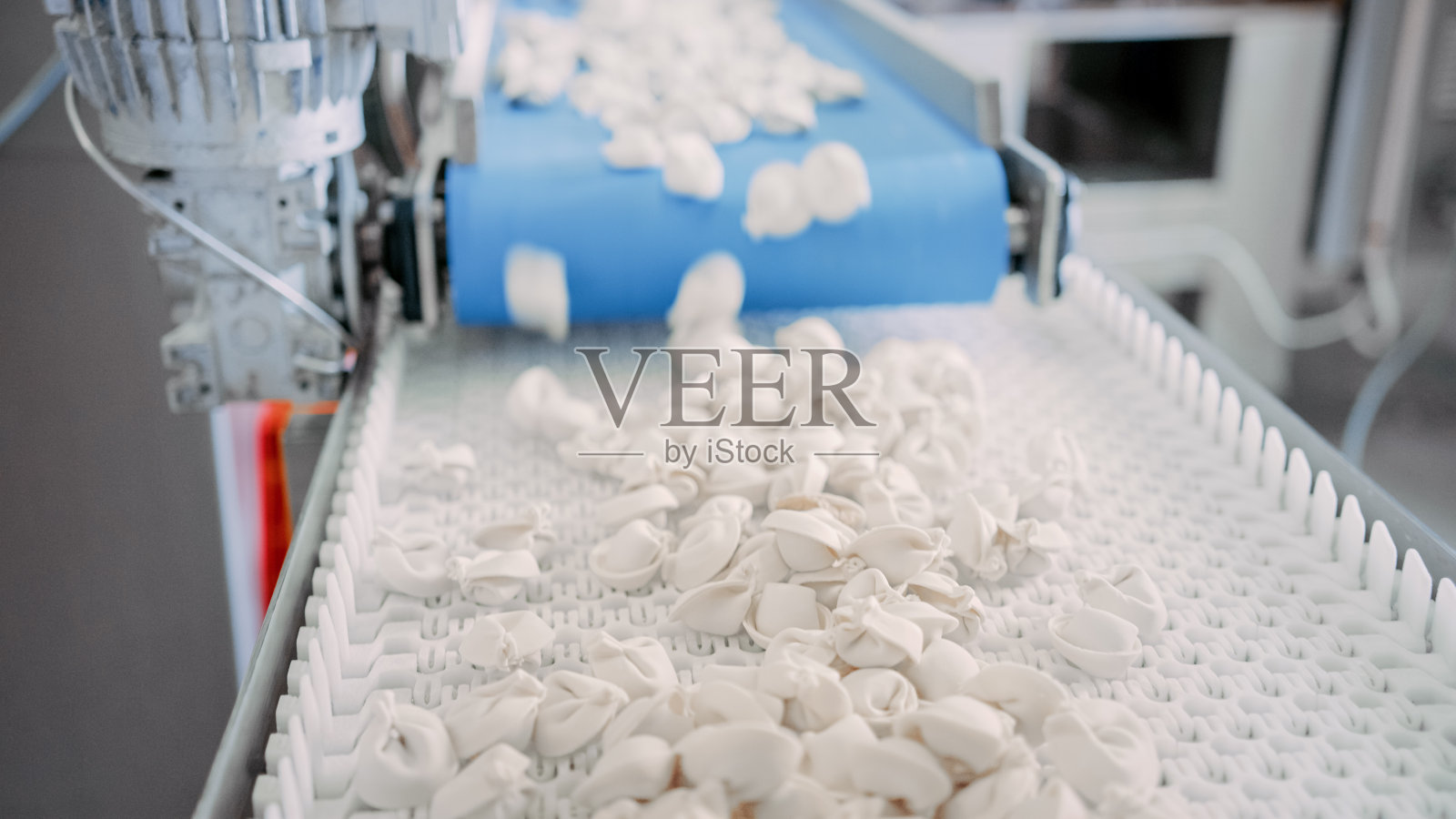 近距离拍摄的自动机器生产过程在饺子工厂。新鲜生Pelmeni落在传送带上。在食品工厂操作的工业机械。照片摄影图片