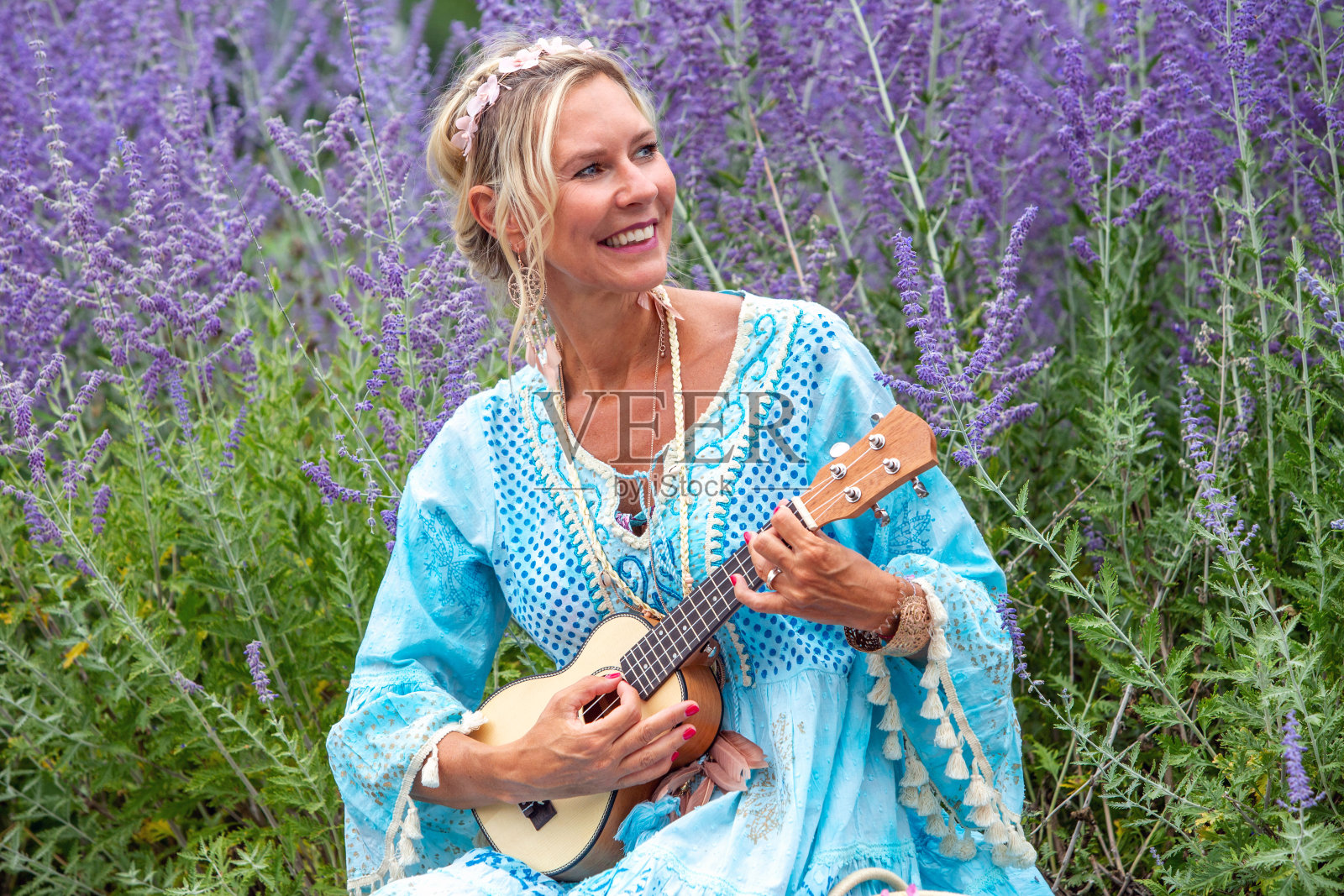 40多岁的金发女人坐在花丛边弹吉他照片摄影图片