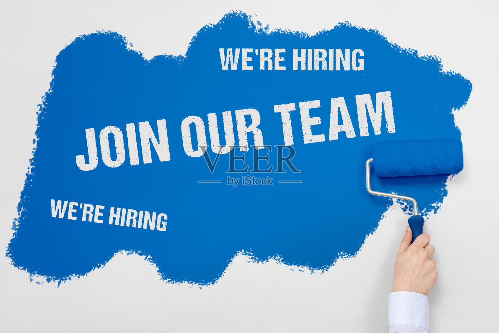 拿着油漆滚轮,用蓝色油漆涂白墙,加入我们的团队,我们正在招聘指示牌照片摄影图片