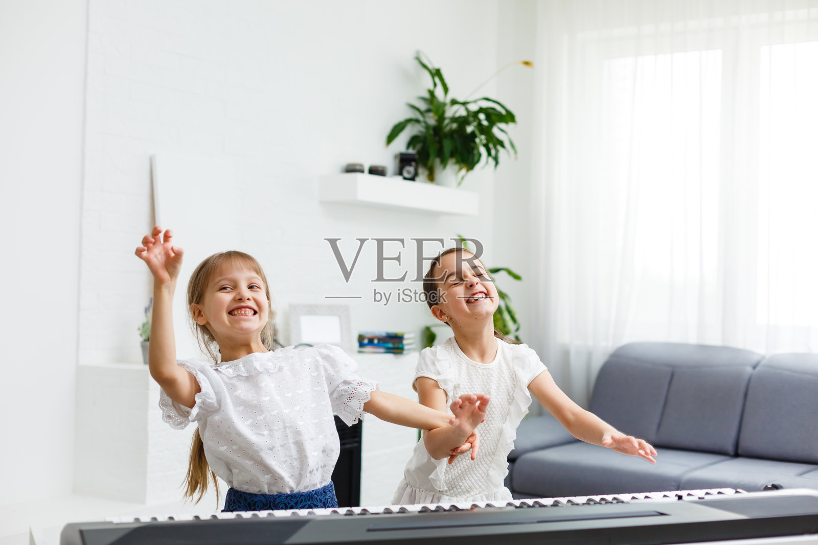 家里的钢琴课。两个女孩在一种乐器上练习乐谱。家庭的概念。隔离期间儿童活动的想法。照片摄影图片