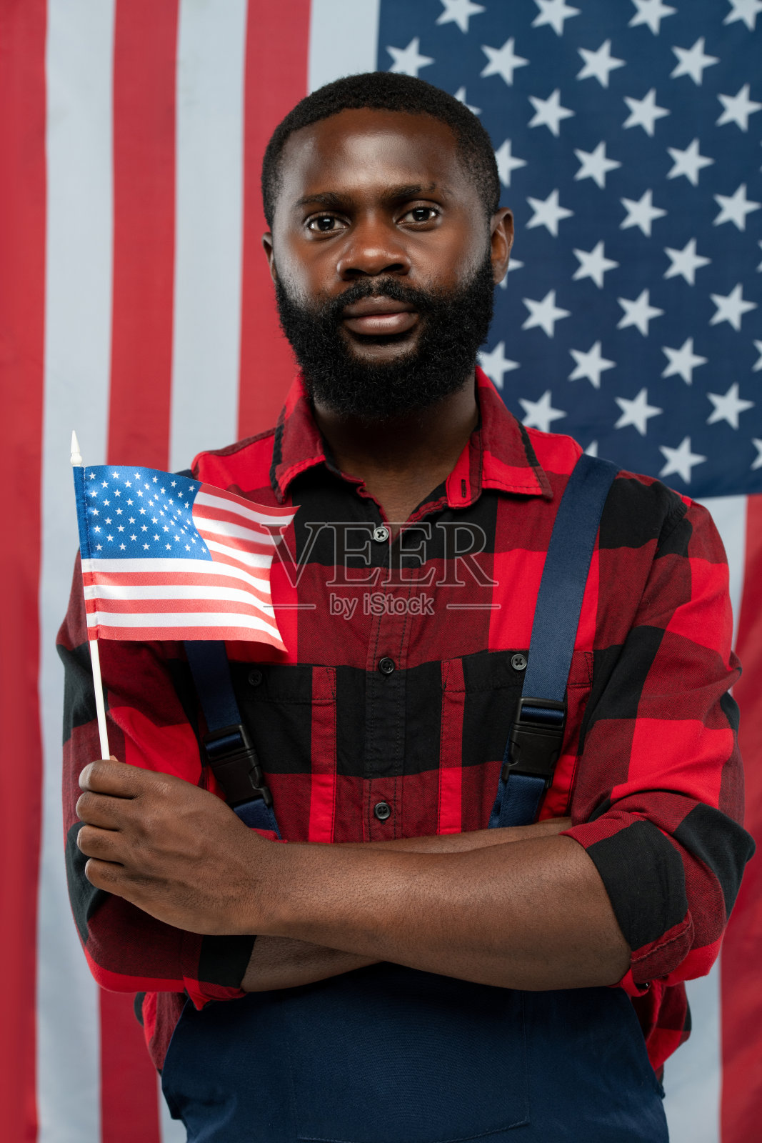 年轻的蓄着胡须的非裔美国工人穿着法兰绒和工装裤为我们举着旗帜照片摄影图片
