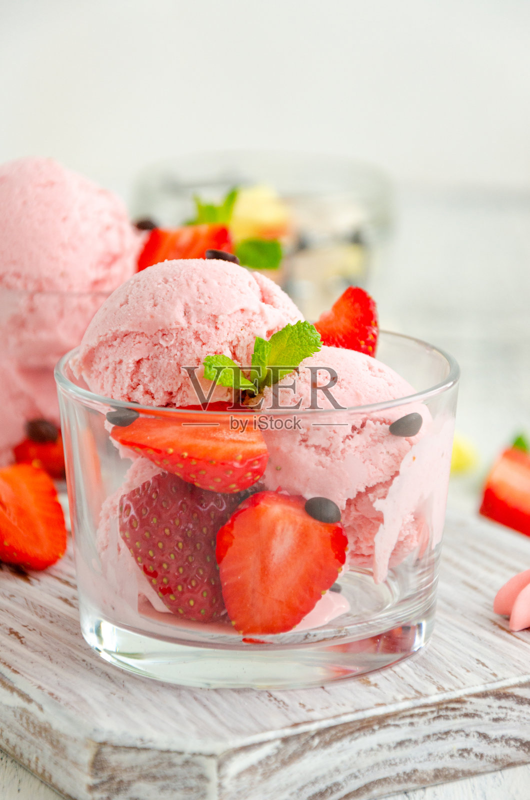 草莓冰淇淋在玻璃杯中,新鲜的草莓,巧克力和薄荷在一个轻木制背景板上。垂直,复制空间。照片摄影图片