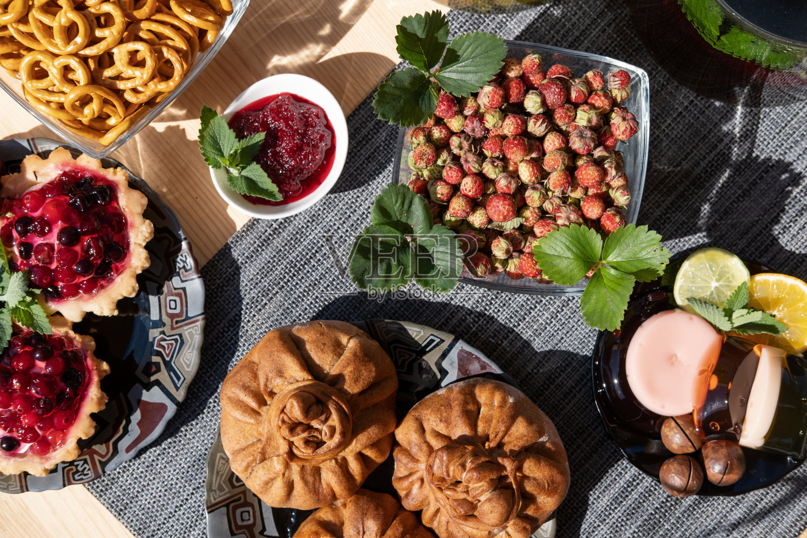 木桌上放着饼干、篮子,篮子里有越桔、馅饼、草莓、水果果冻、蛋糕和天然草药茶。在户外阳光早餐照片摄影图片