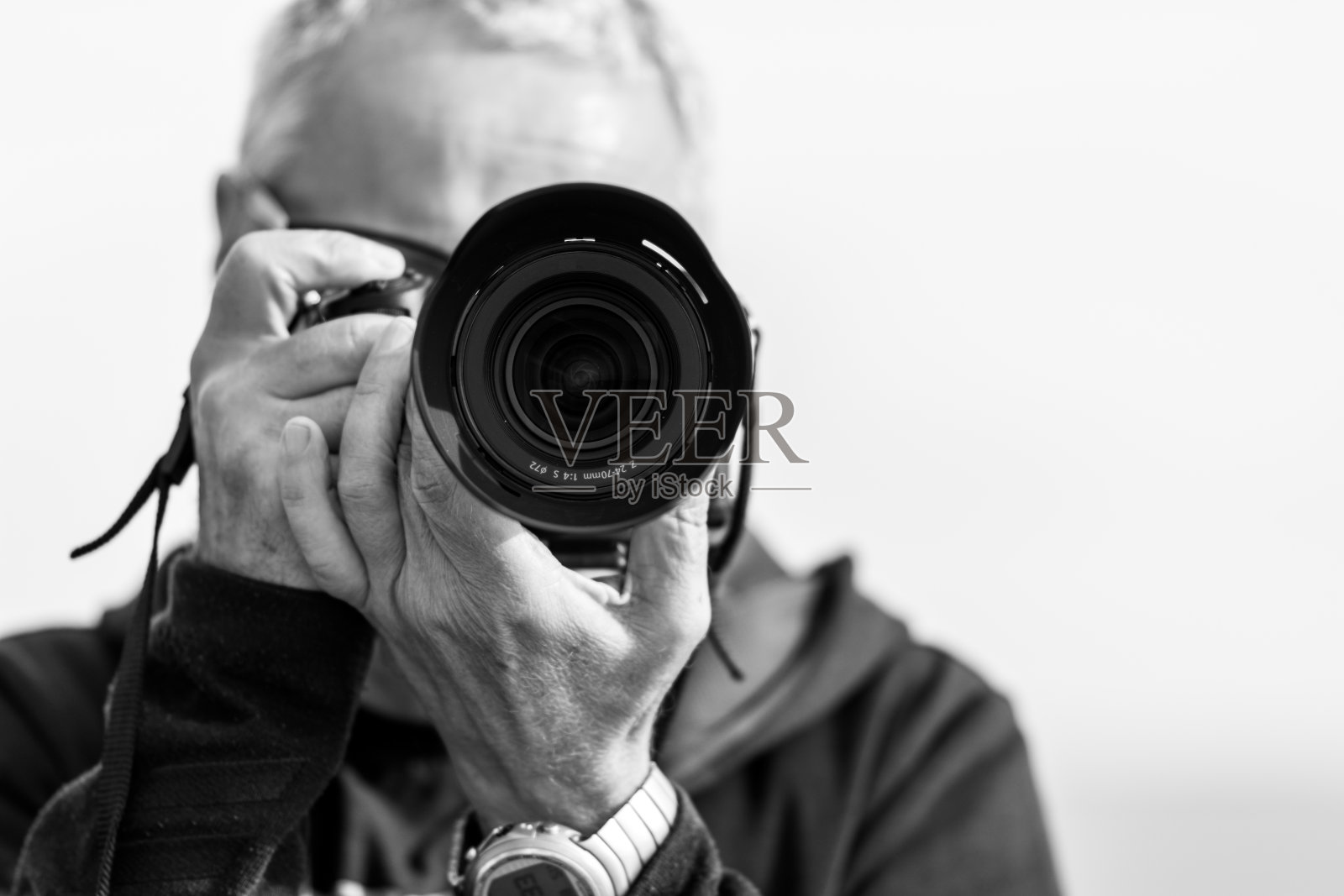 一张50多岁中年男子的黑白照片,用现代无反光镜相机拍照,照片遮住了他的脸。背景是蓝色朦胧的天空照片摄影图片