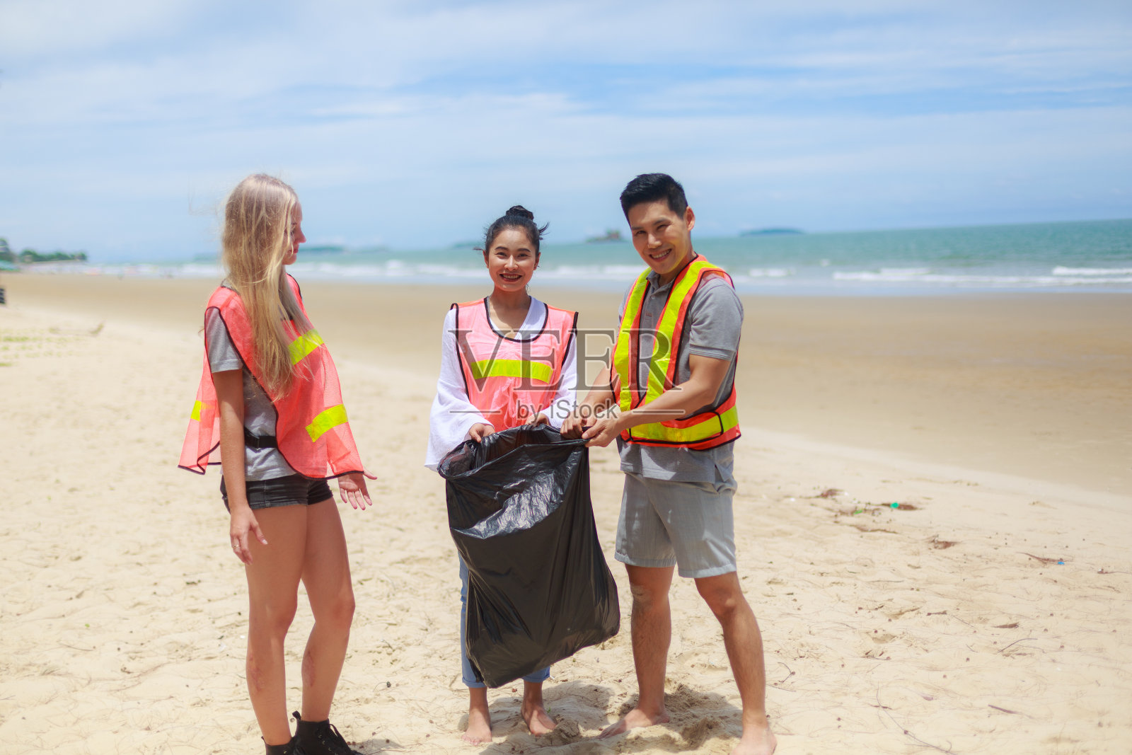 一群义工捡垃圾到塑胶袋里,准备早上清理海滩。志愿者的概念。照片摄影图片