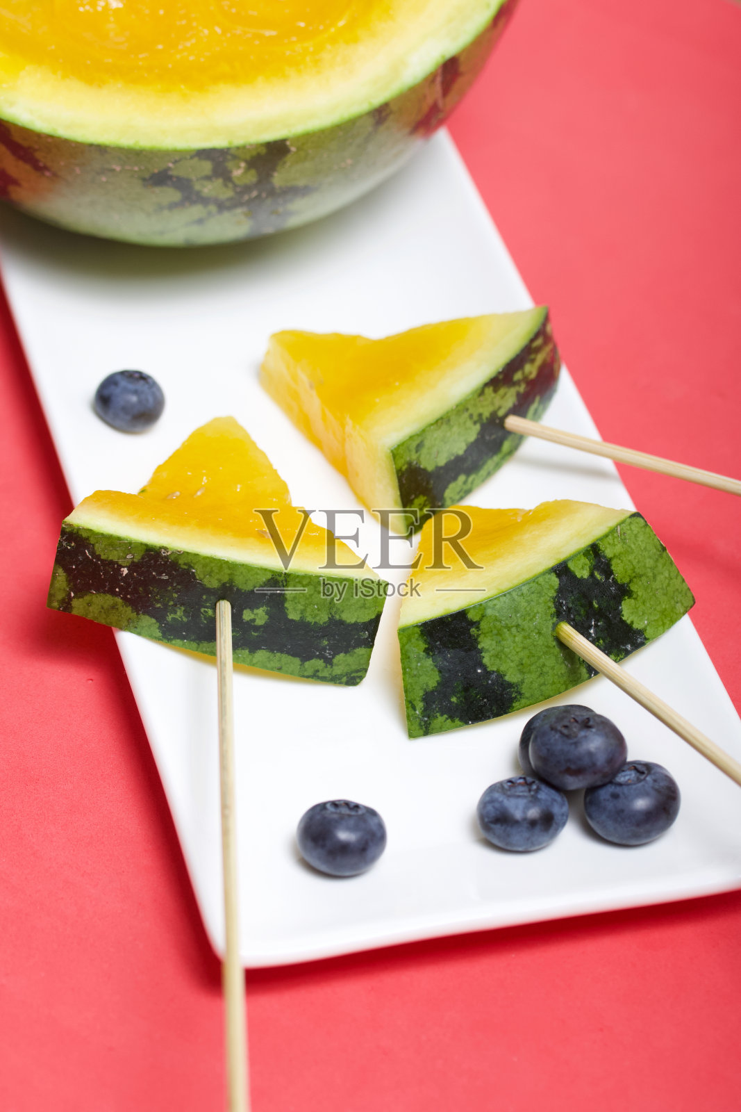 黄西瓜条。躺在盘子上。附近的蓝莓。镶在珊瑚色表面上的盘子。照片摄影图片