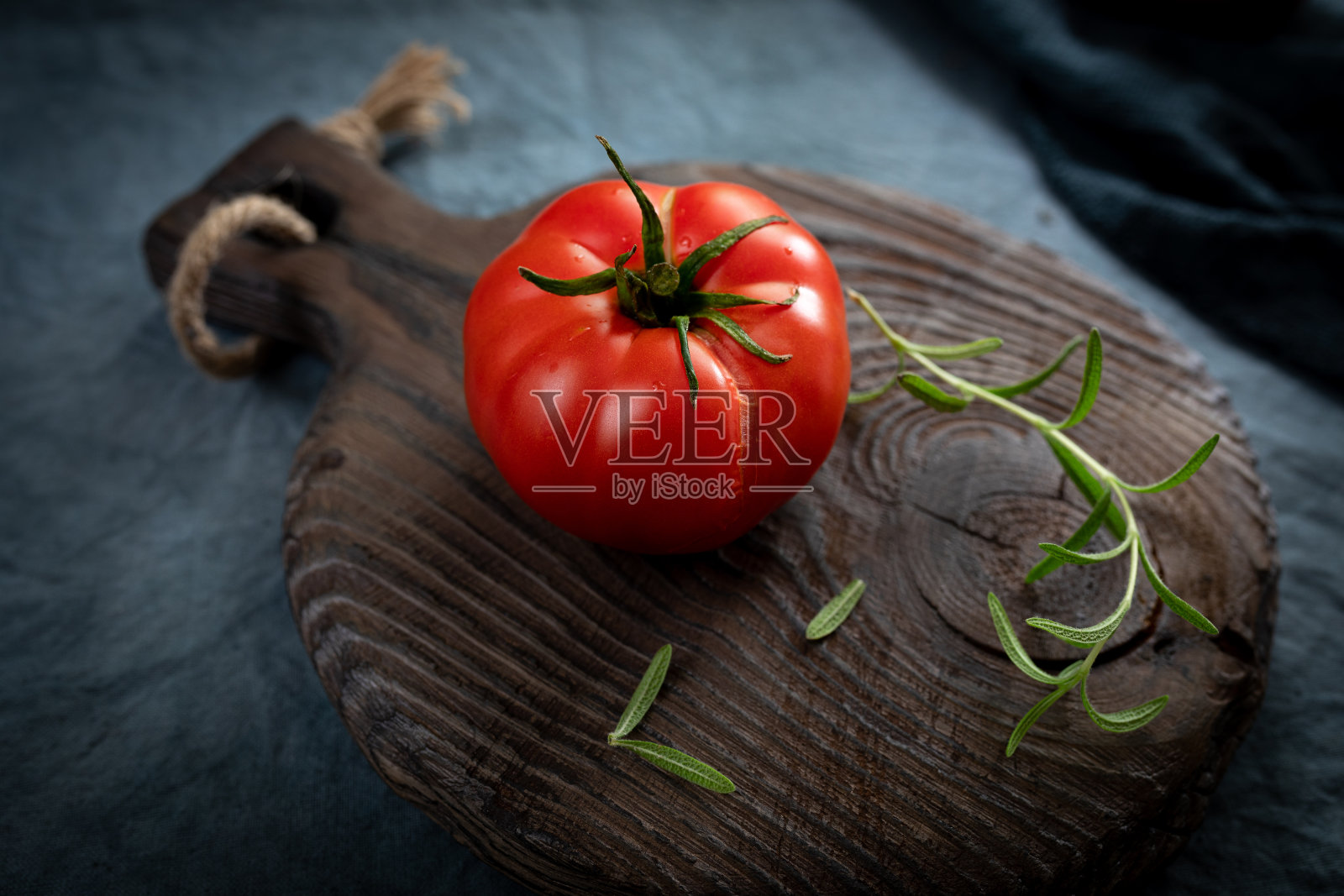 熟透的有机番茄和迷迭香放在旧砧板上。成熟的蔬菜被榨成汁。选择性地聚焦在裂缝上。照片摄影图片