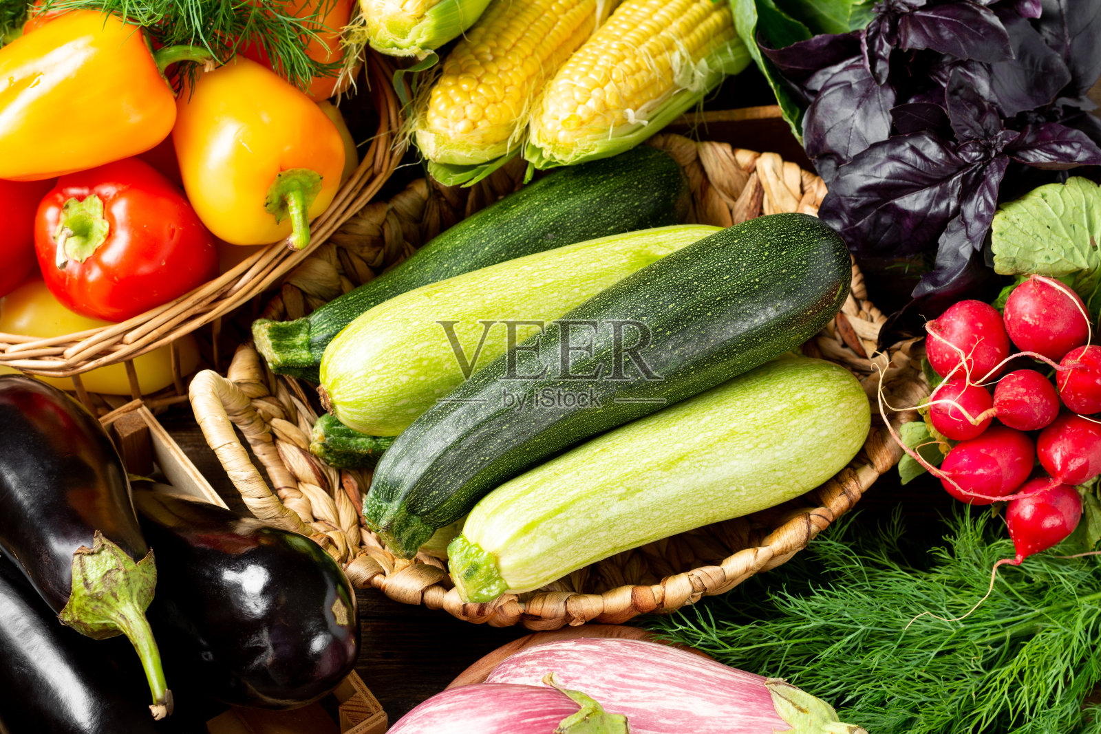 桌上的木盒里装着各种各样的蔬菜。篮子里有很多不同的生蔬菜。桌上有西葫芦、萝卜、茄子、玉米、大蒜、辣椒和茄子。健康食品的概念照片摄影图片