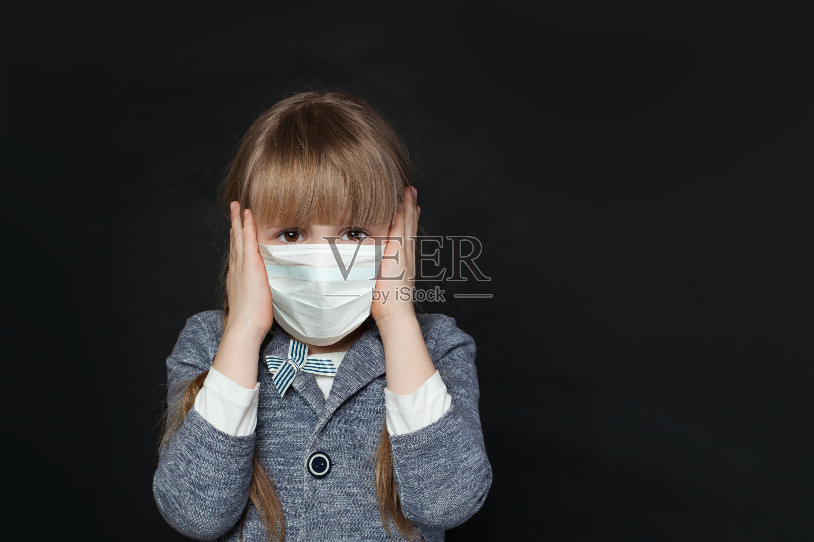 不幸的女童戴着医用防护口罩,遮住了耳朵照片摄影图片