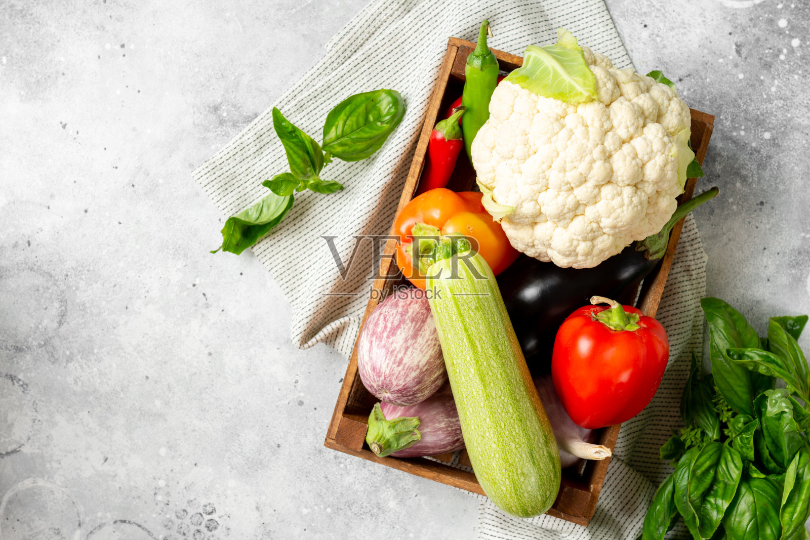 装在木盒里的各种蔬菜。盒子里有很多不同的生蔬菜。桌上有花椰菜、西葫芦、大蒜、甜椒和茄子。健康饮食的概念照片摄影图片