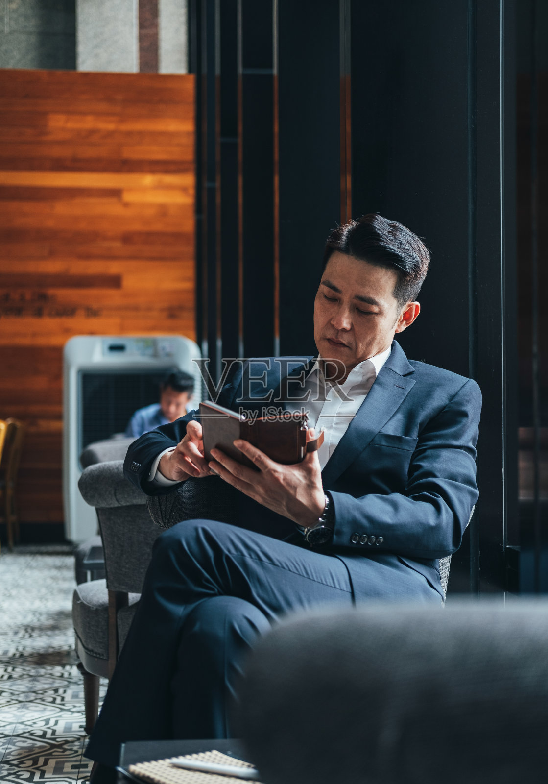 一个商人坐在咖啡馆里,手里拿着一个手机照片摄影图片