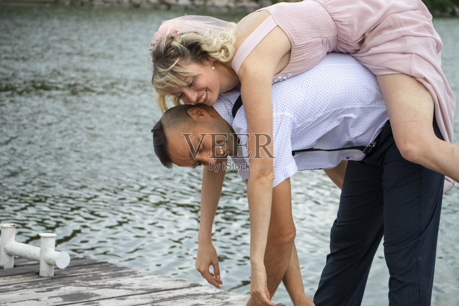 创意潮人的海边婚礼。新娘身着粉色的婚纱和面纱,新郎则穿着漂亮的吊带裤和年轻的衬衫。疯狂,有趣和不寻常的婚姻方式照片摄影图片