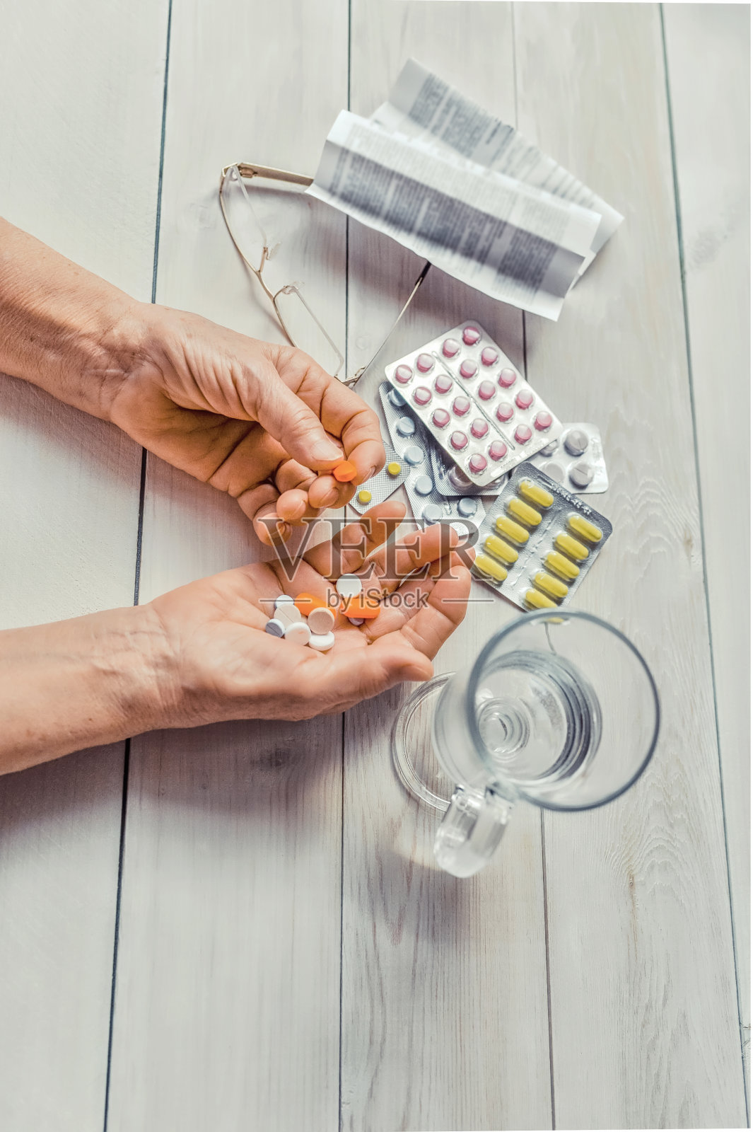 老者手里拿着药,桌上放着一杯水。照片摄影图片