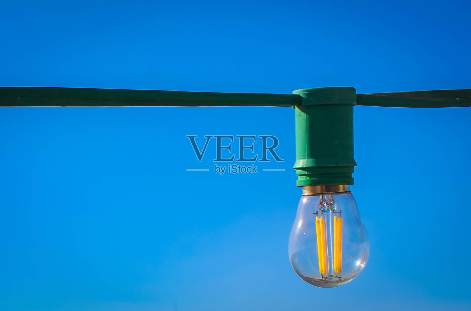 一个透明的灯泡在一根绿色的电线上靠近蓝色的天空照片摄影图片