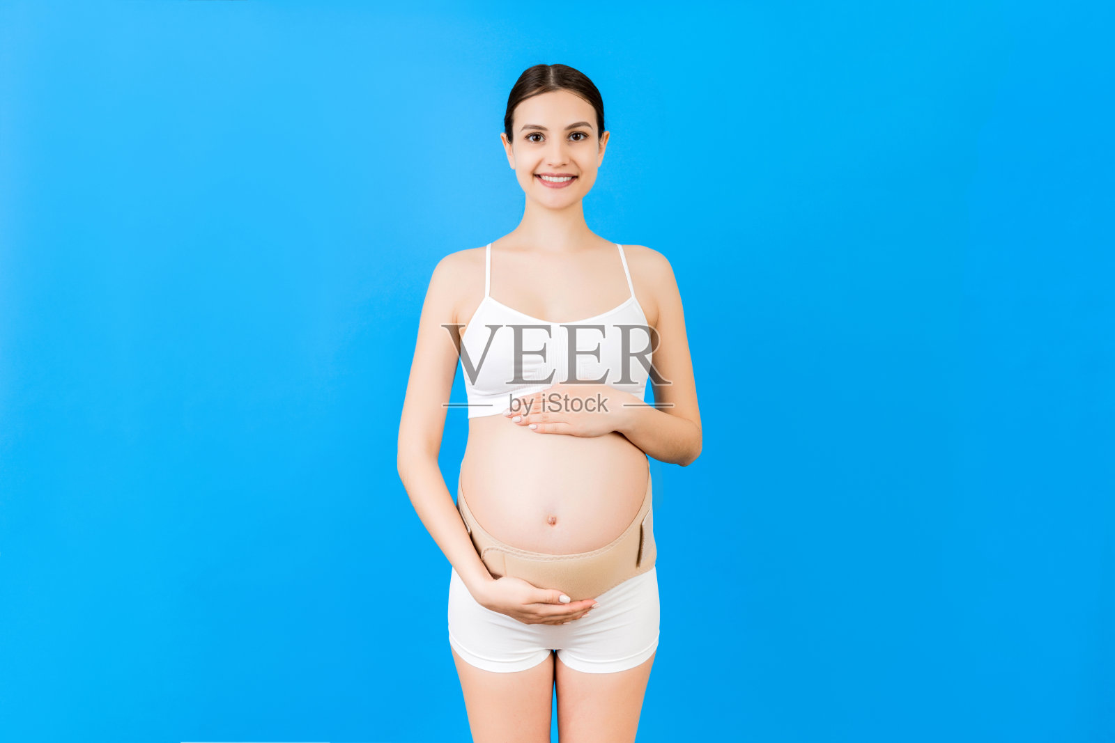 肖像的弹性孕妇带穿着内衣孕妇,以减少背痛在蓝色背景与复制空间。骨科腹部支撑带概念照片摄影图片