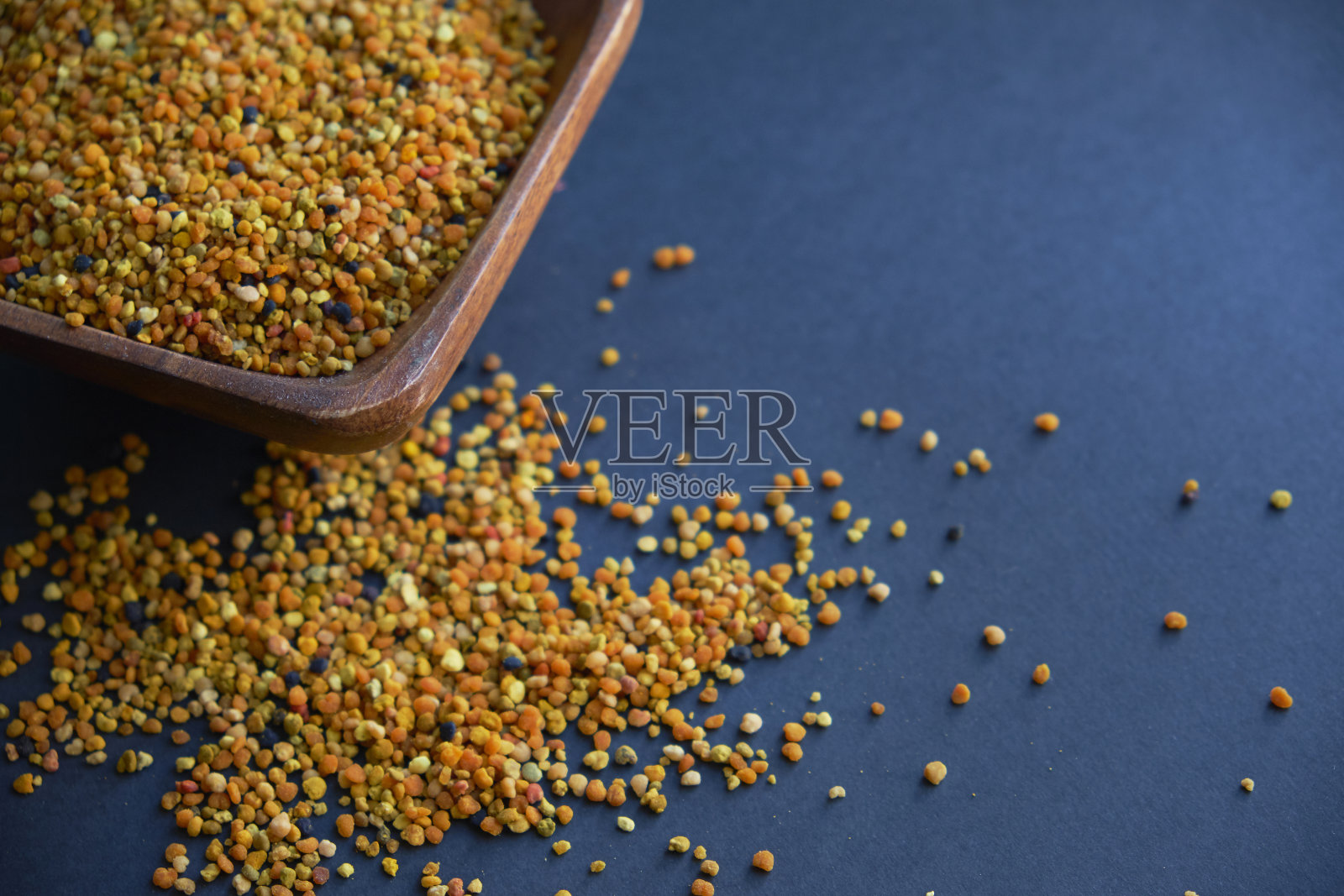 木勺里的蜂花粉是健康食品的补充。黑色表背景。工蜂从地里采集的花粉的球状或小球照片摄影图片