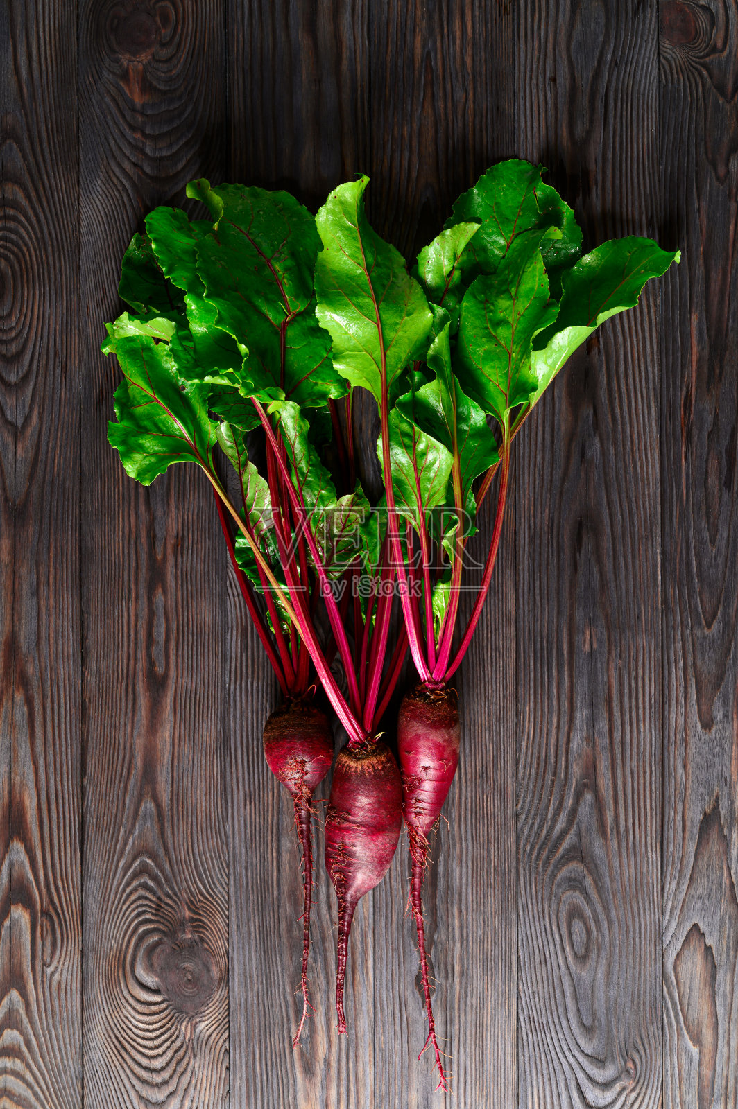 黑色木质背景上的绿色顶部的生甜菜。生态食品,乡村风格。照片摄影图片