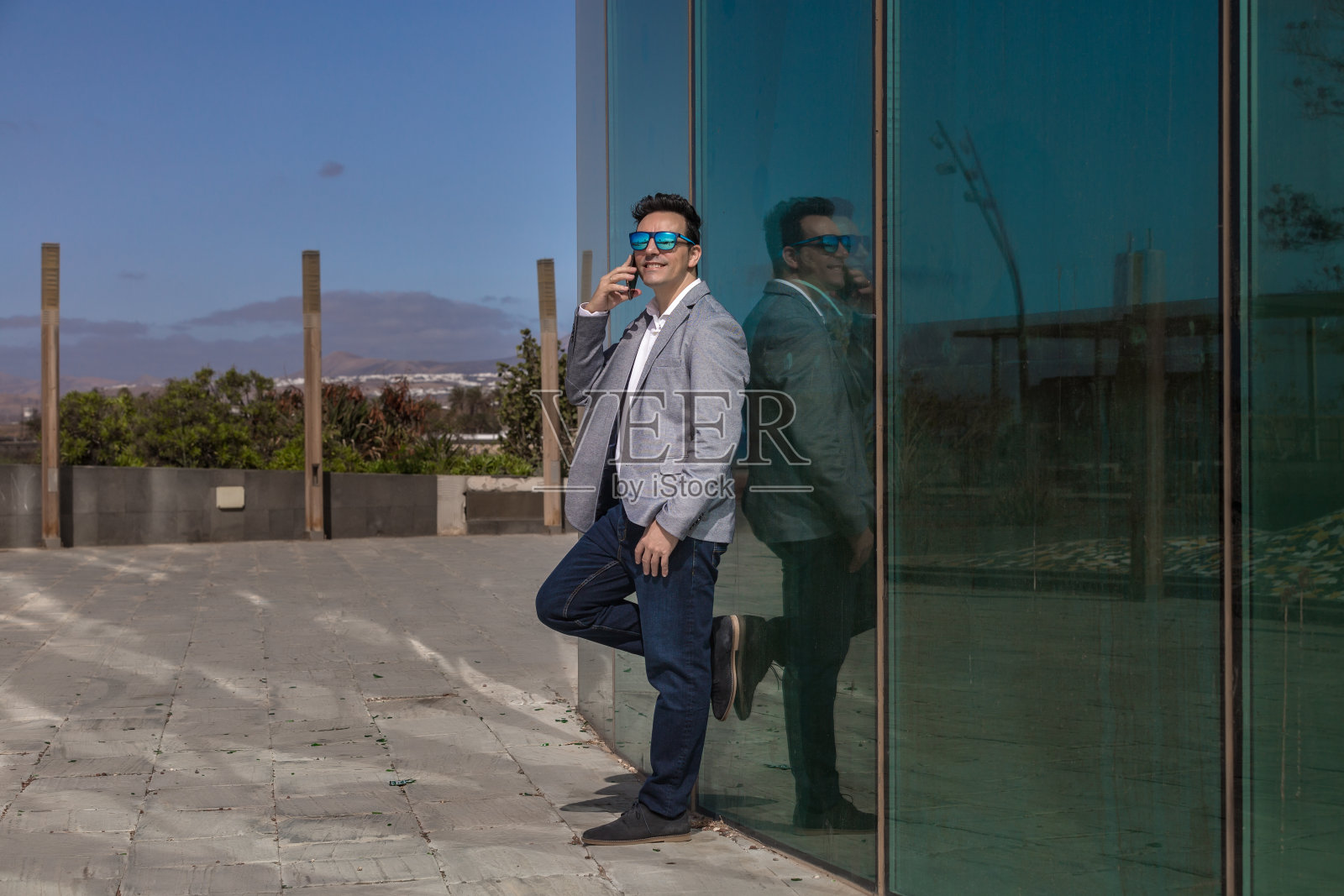 积极的商人在玻璃墙附近的智能手机上讲话照片摄影图片